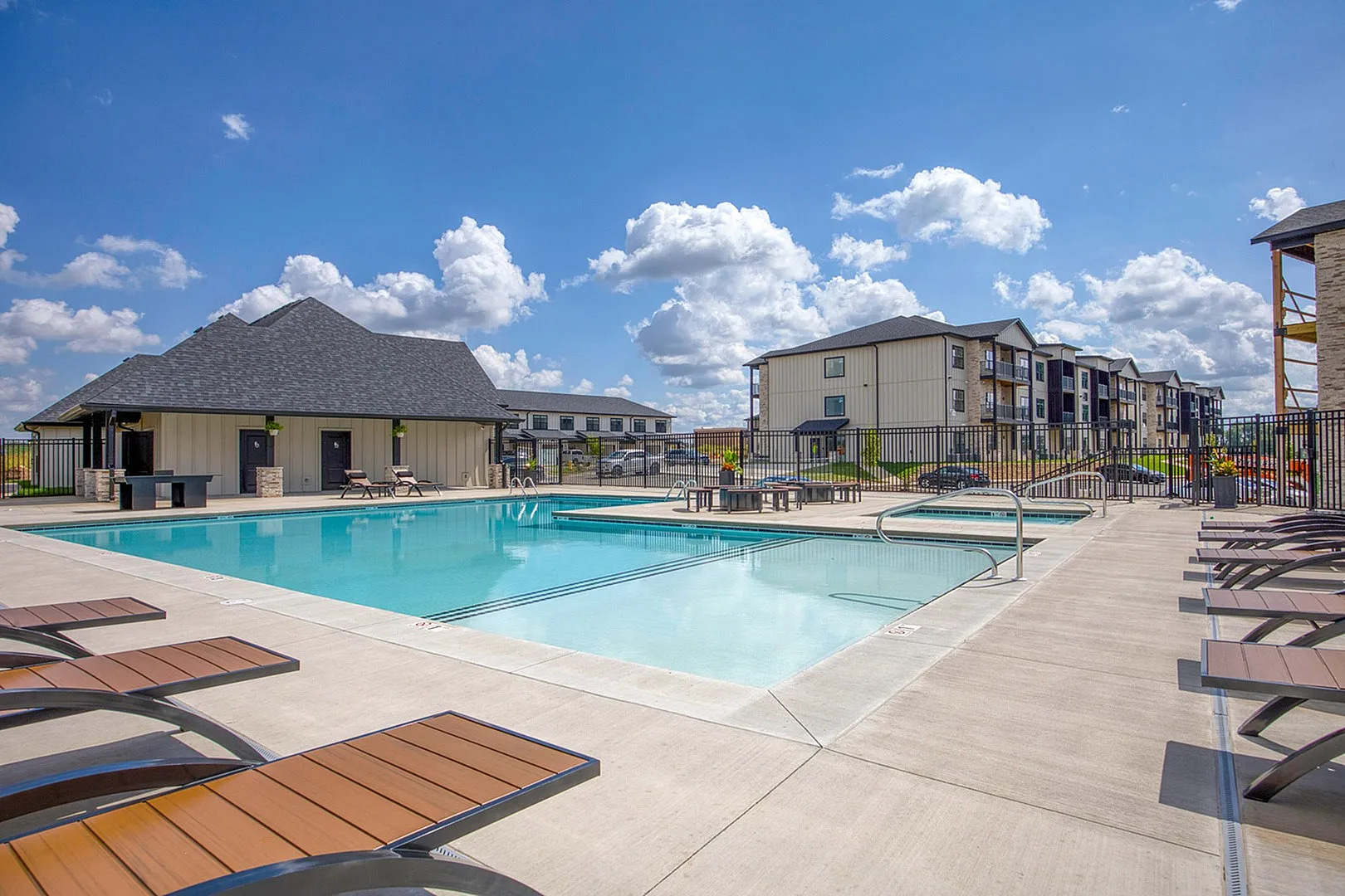Luxurious apartment complex with a sparkling outdoor pool, comfortable sun loungers, and modern architecture under a vibrant blue sky.