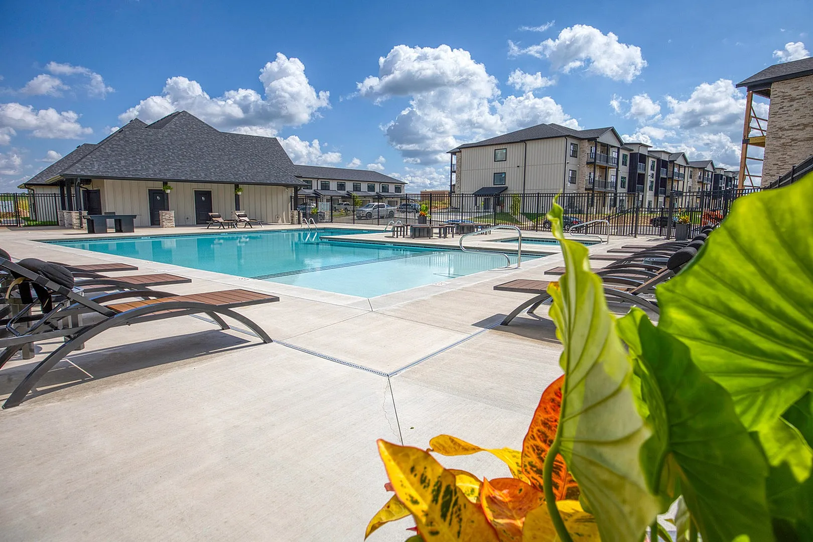 Inviting pool area with modern sun loungers and picturesque views of residential apartments under a bright blue sky.