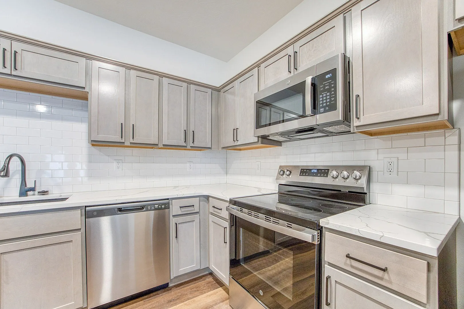 Modern kitchen with sleek stainless steel appliances, elegant white subway tile backsplash, and stylish gray cabinetry complemented by marble countertops.