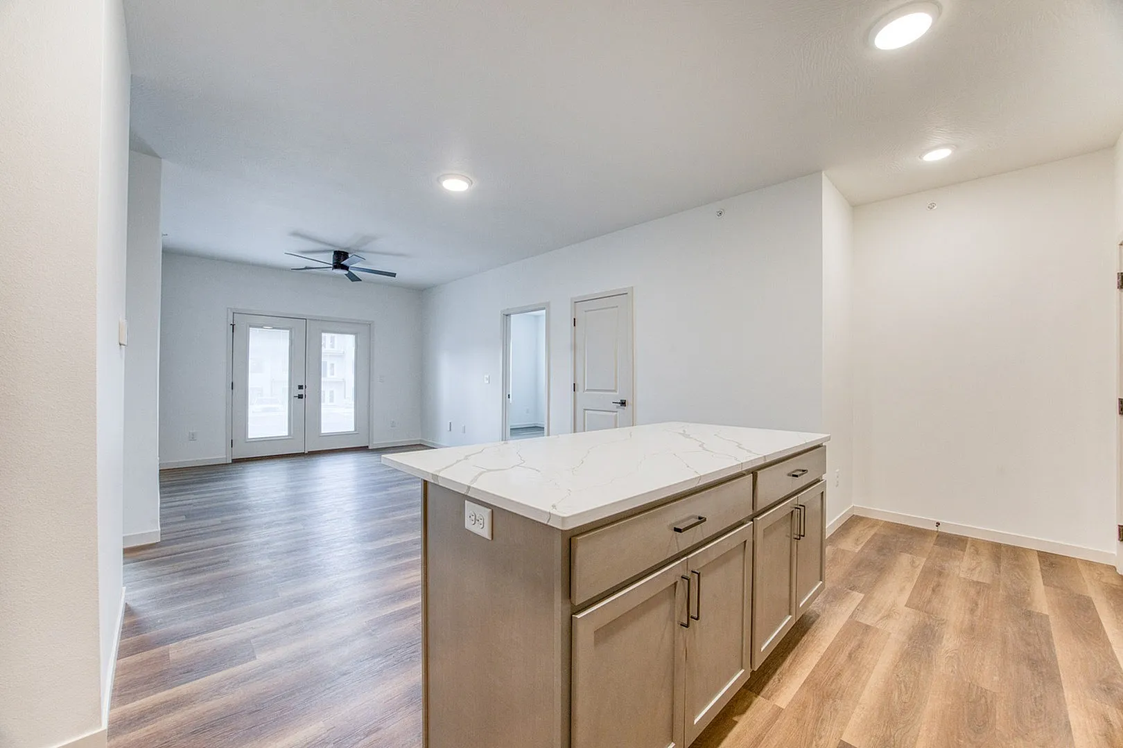 Modern open-plan living area with elegant wood flooring, stylish kitchen island, and bright natural light through French doors.