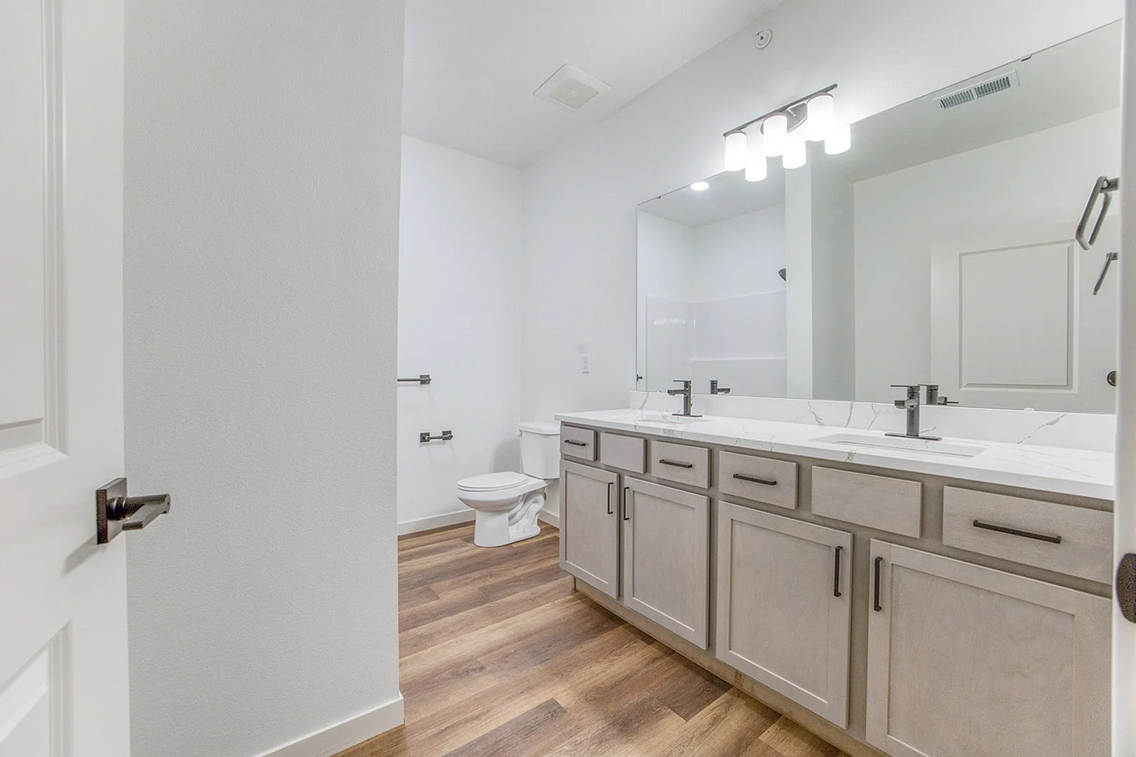 Elegant bathroom featuring dual sinks, a large mirror, and chic wood flooring.