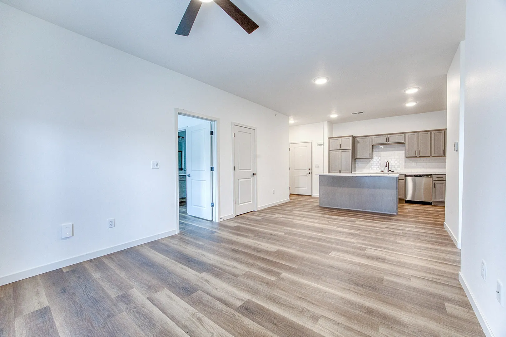 Bright open-plan living area with elegant wood flooring, modern kitchen with sleek cabinetry, and ceiling fan enhancing comfort.