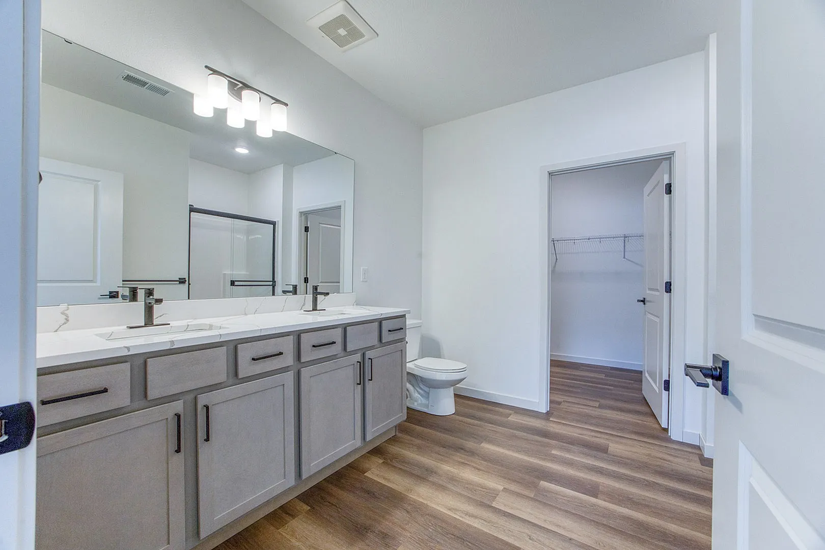 Modern bathroom featuring a double sink vanity with sleek fixtures, elegant lighting, and a spacious walk-in closet.