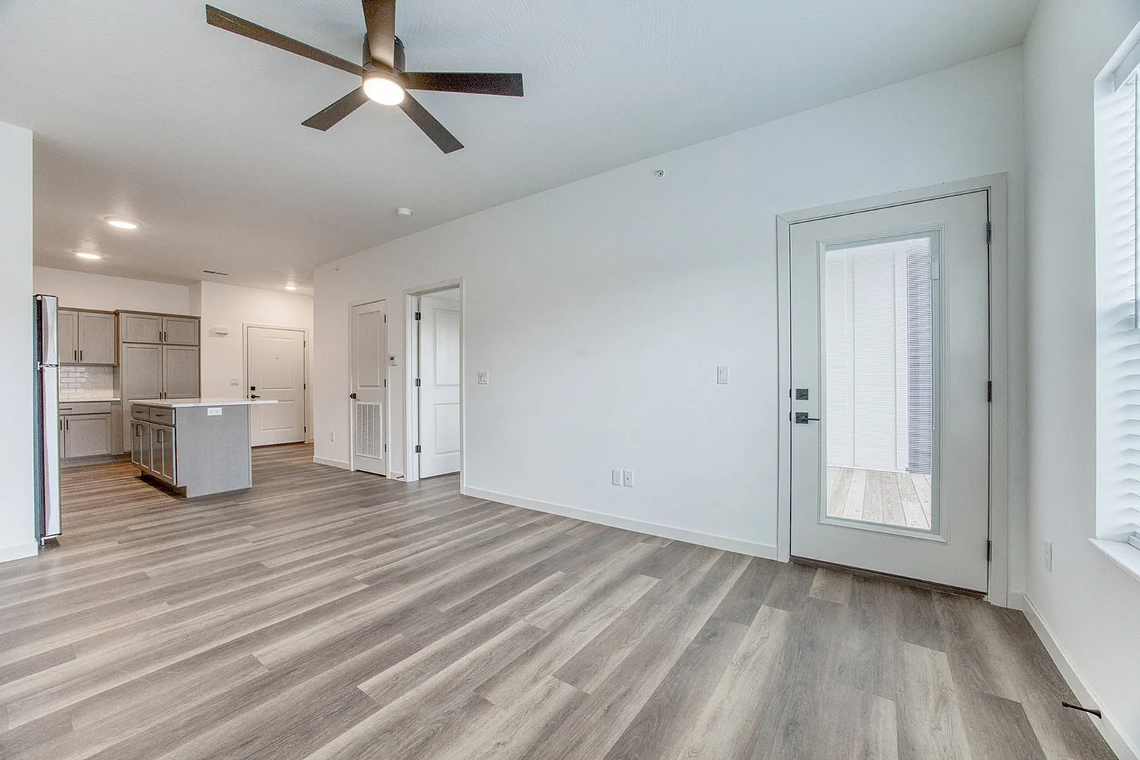 Bright and modern open-concept apartment showcasing sleek laminate flooring, a contemporary ceiling fan, and a spacious kitchen with stylish cabinetry.