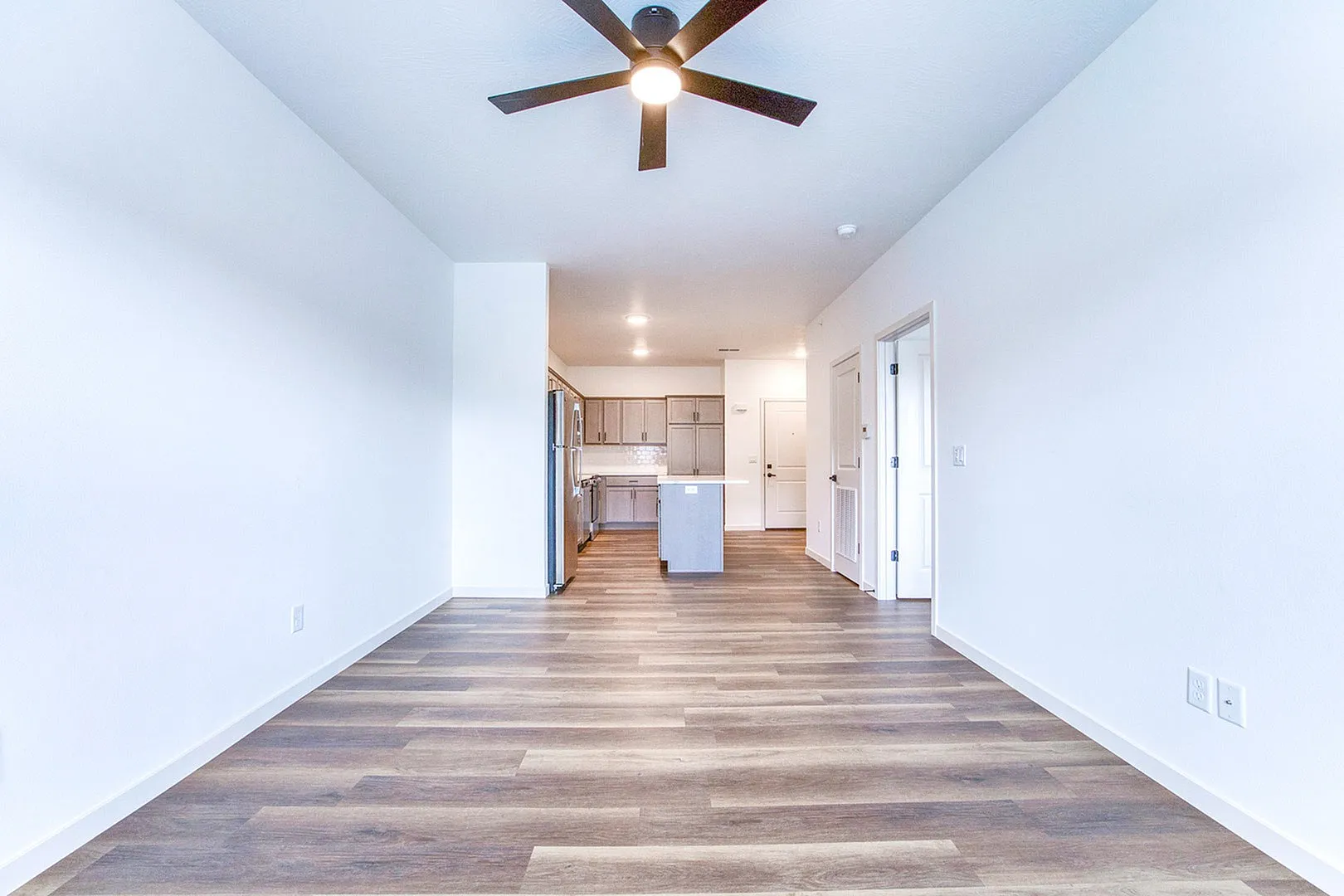 Modern open-concept apartment featuring sleek wood flooring, a stylish ceiling fan, and a spacious kitchen with stainless steel appliances.