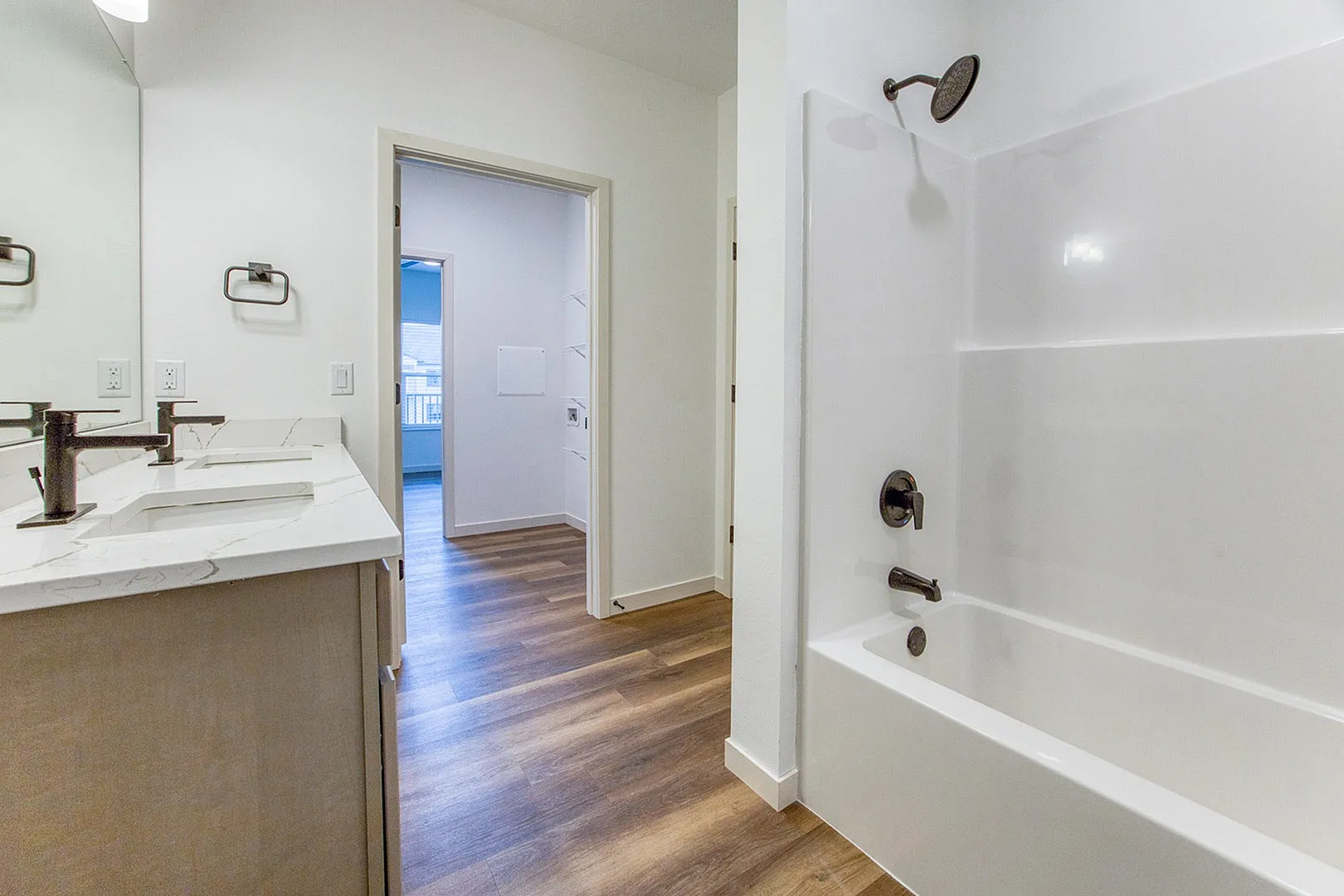 Modern bathroom featuring a sleek white bathtub, elegant marble countertop with dual sinks, and inviting laminate flooring.