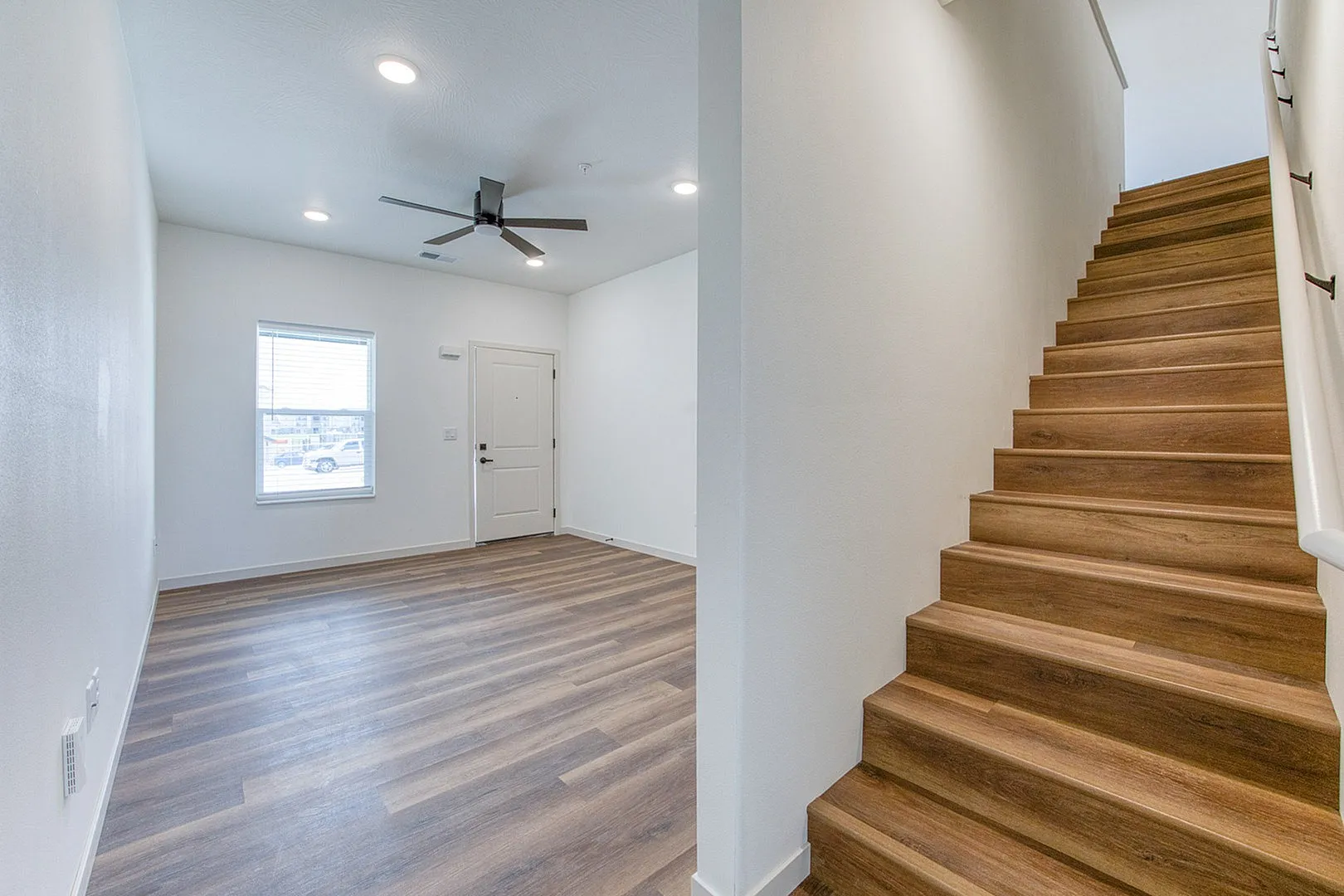 Bright and inviting entryway with modern wooden flooring, sleek ceiling fan, and elegant staircase leading to upper levels, perfect for a stylish living experience.