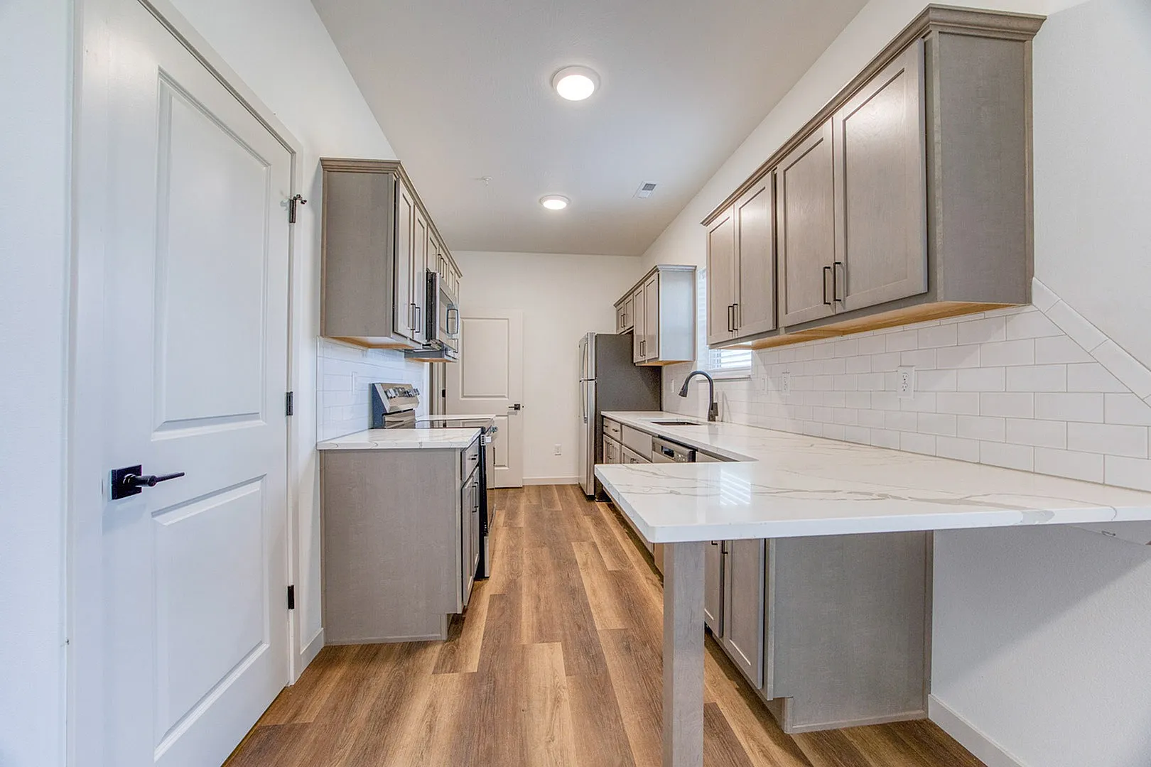 Modern kitchen featuring sleek gray cabinetry, pristine white countertops, and warm wood flooring.