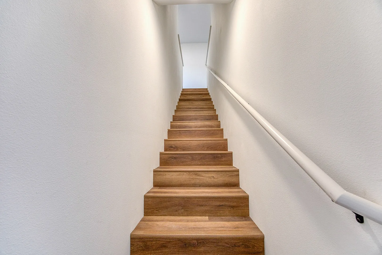 Inviting wooden staircase with sleek white walls offering a warm welcome to the upper levels of a modern home.