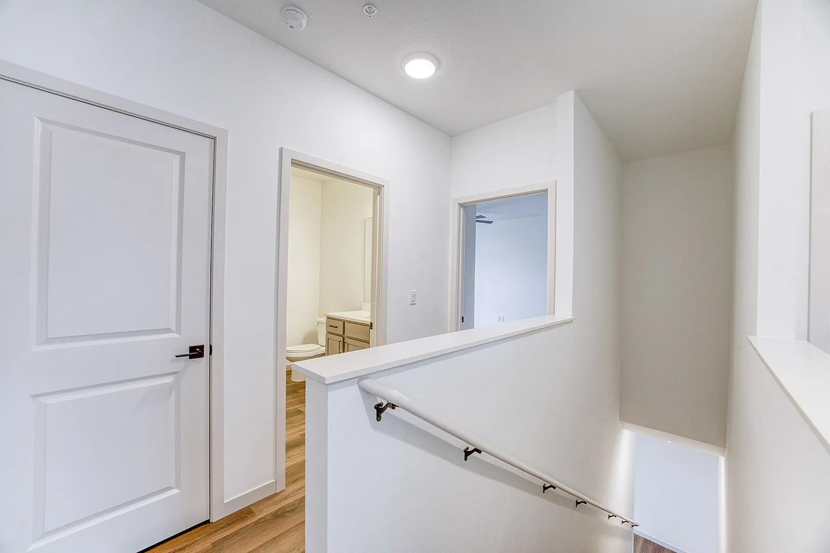 Bright hallway with wooden flooring leading to a modern bathroom, featuring a sleek handrail design.
