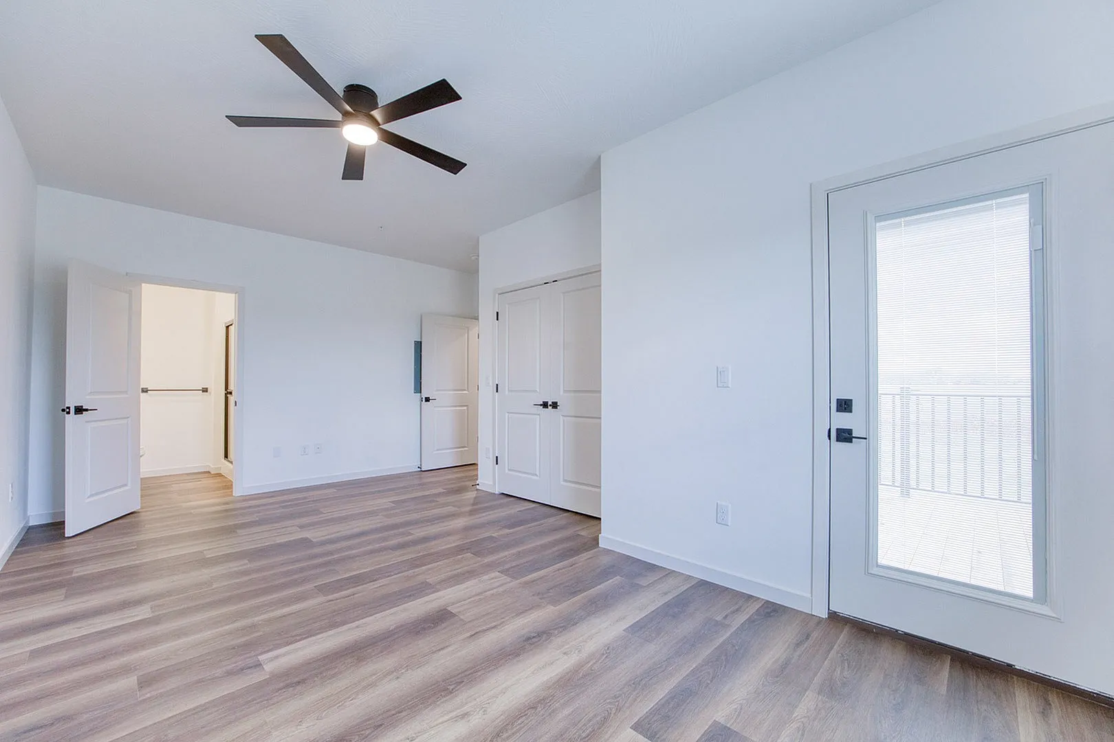 Bright and spacious bedroom with elegant hardwood flooring, modern ceiling fan, and access to a private balcony.