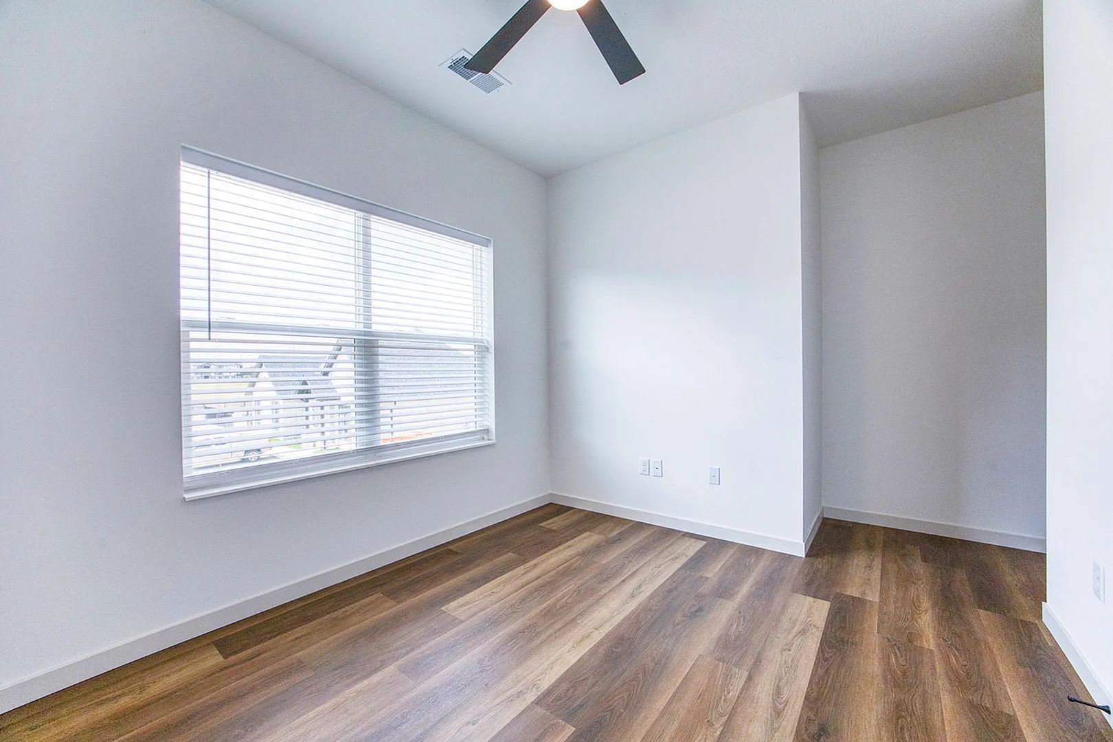 Bright modern room with elegant wood flooring and a large window featuring stylish blinds, perfect for creating a cozy living area.