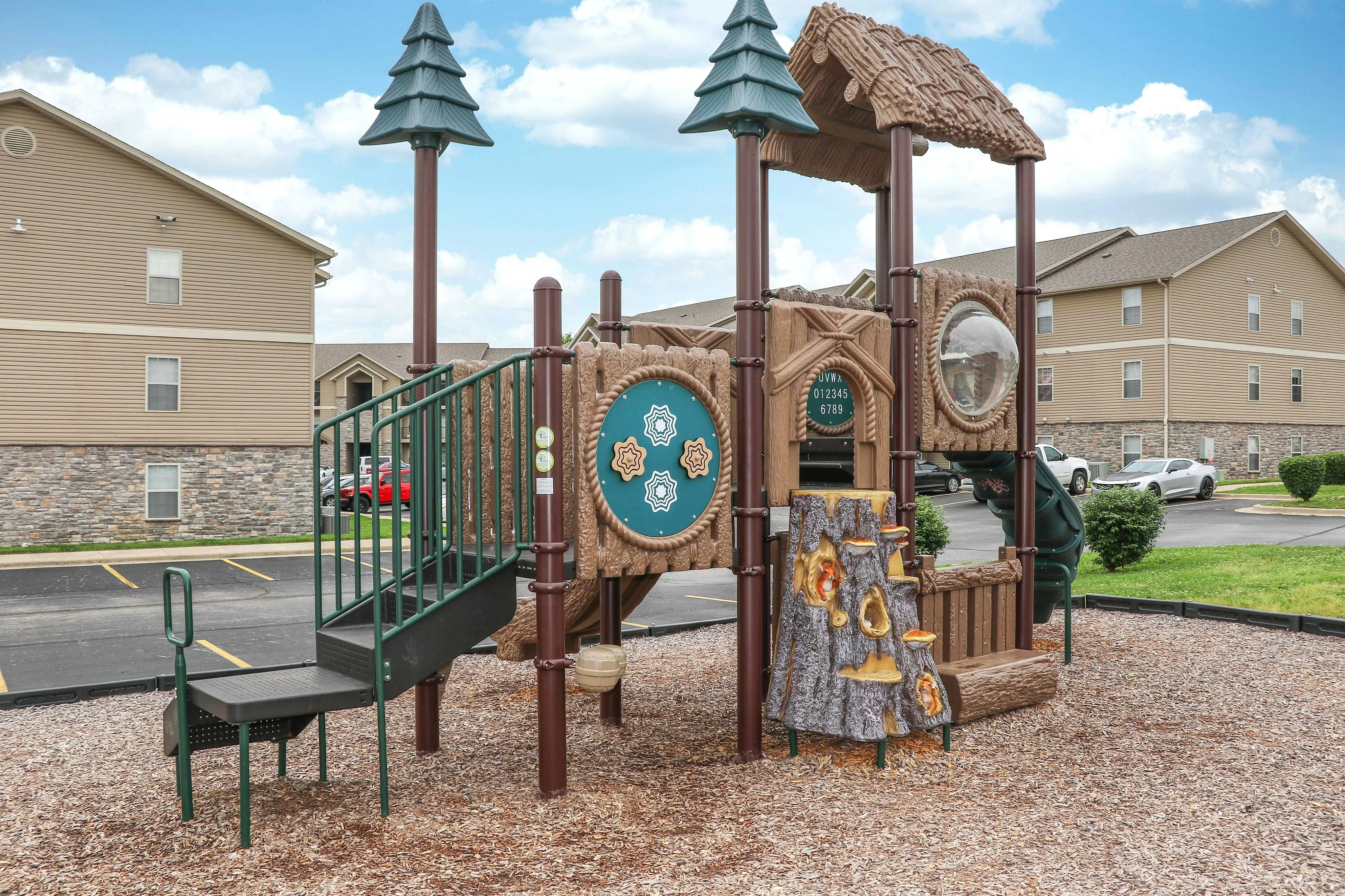 Charming apartment playground with whimsical treehouse design, nestled in a welcoming community with modern buildings in the background.