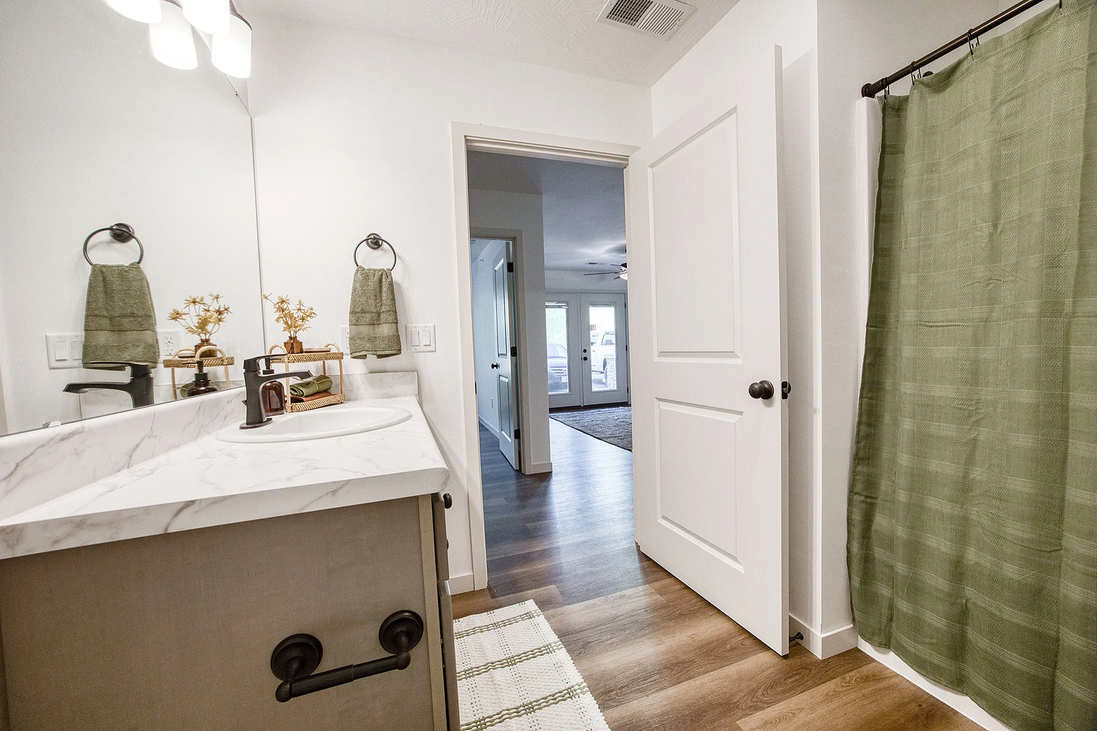 Chic bathroom with marble countertop, elegant fixtures, and green accents leading to a bright, open living space.
