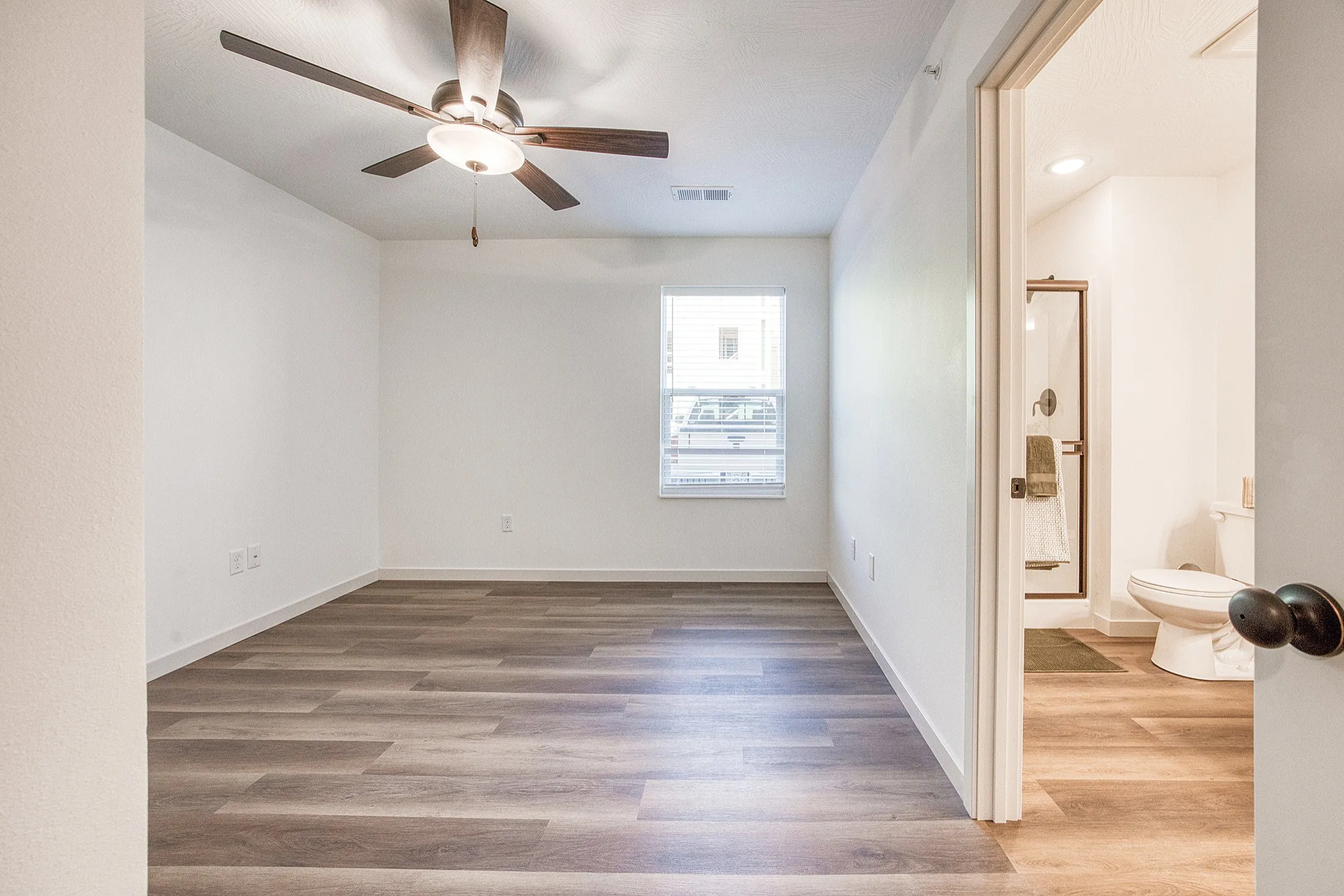 Bright and inviting bedroom featuring elegant wood flooring, a modern ceiling fan, and access to a private bathroom.
