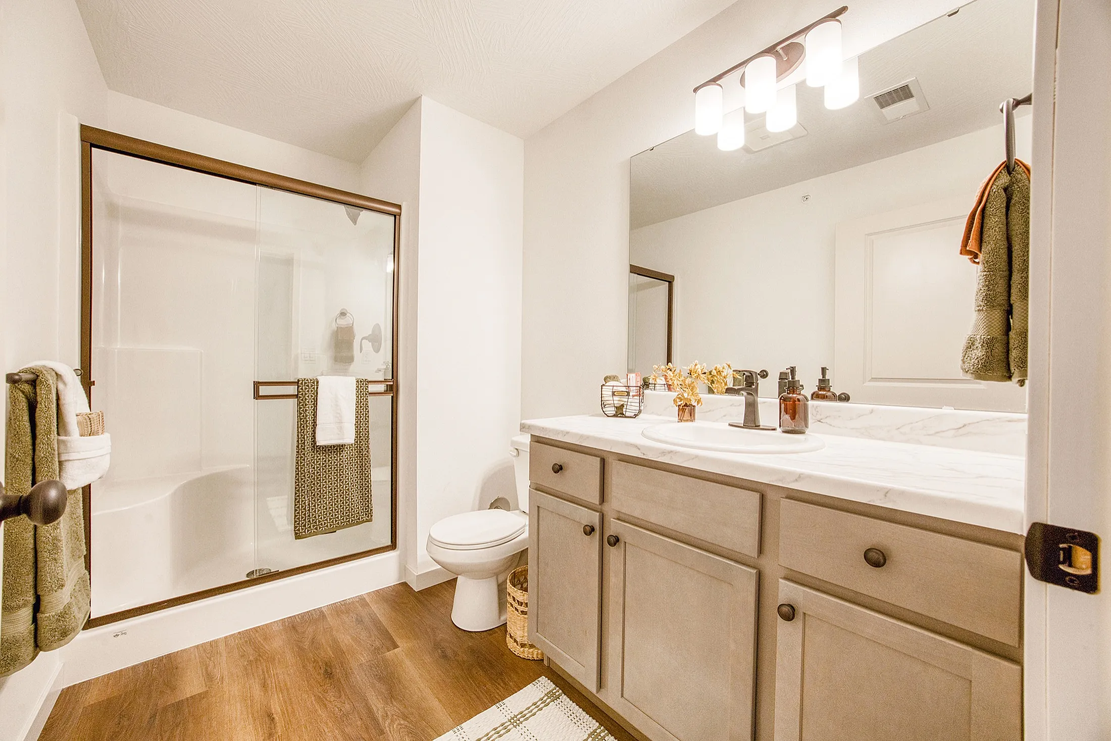 Elegant bathroom with modern glass shower, sleek marble countertops, and warm wooden flooring.