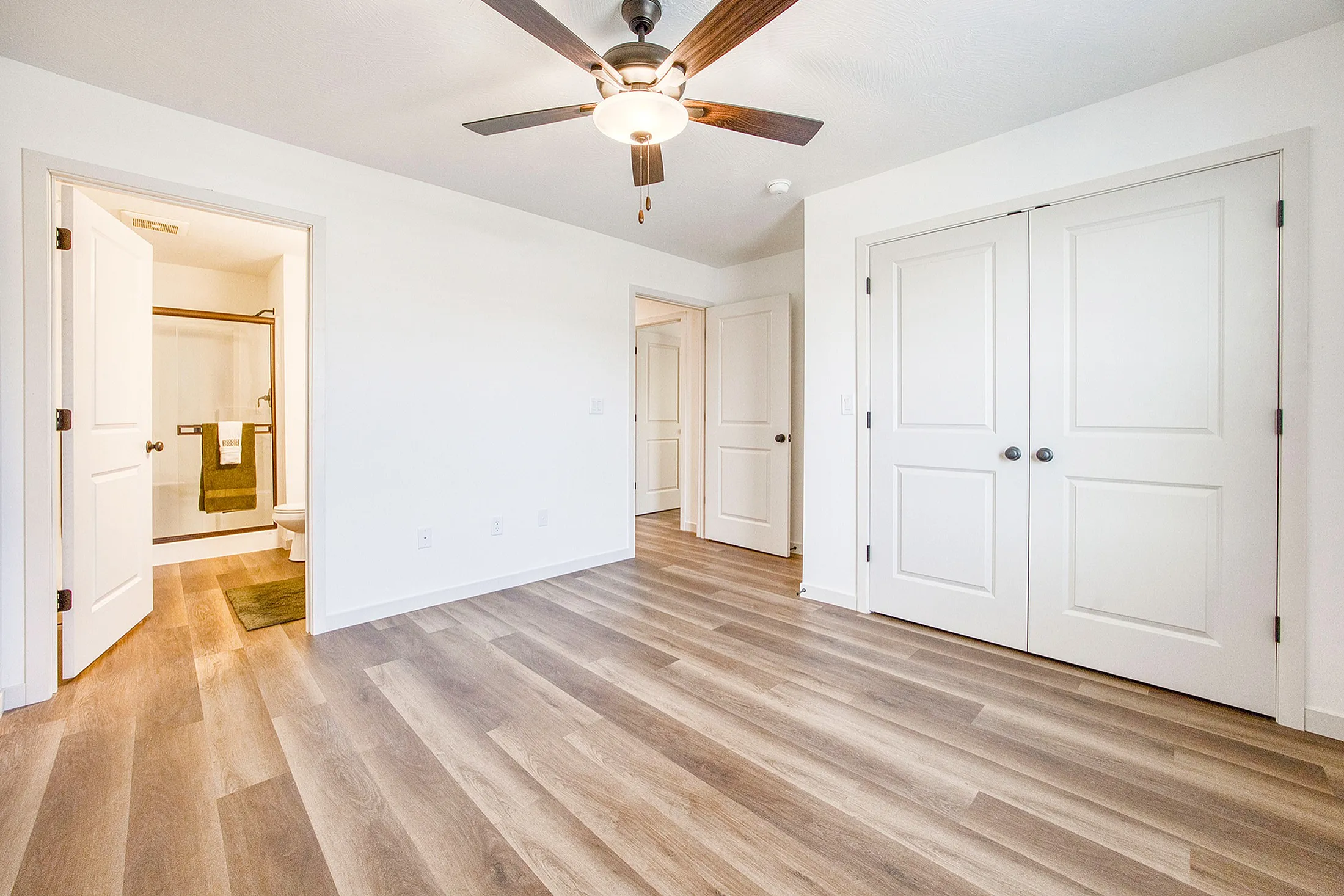 Bright, spacious bedroom with elegant wood flooring and a modern ceiling fan, leading to a stylish en-suite bathroom.