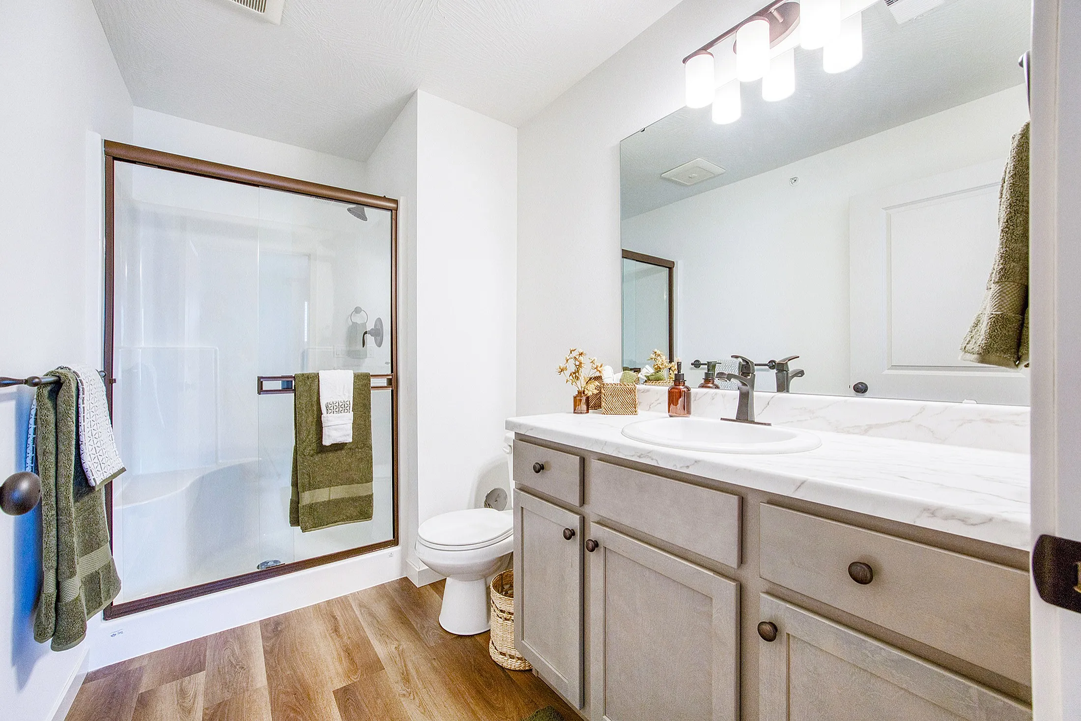 Modern bathroom with a glass-enclosed shower, elegant wood cabinetry, and sleek countertop. Bright lighting and tasteful decor create a luxurious and inviting atmosphere.