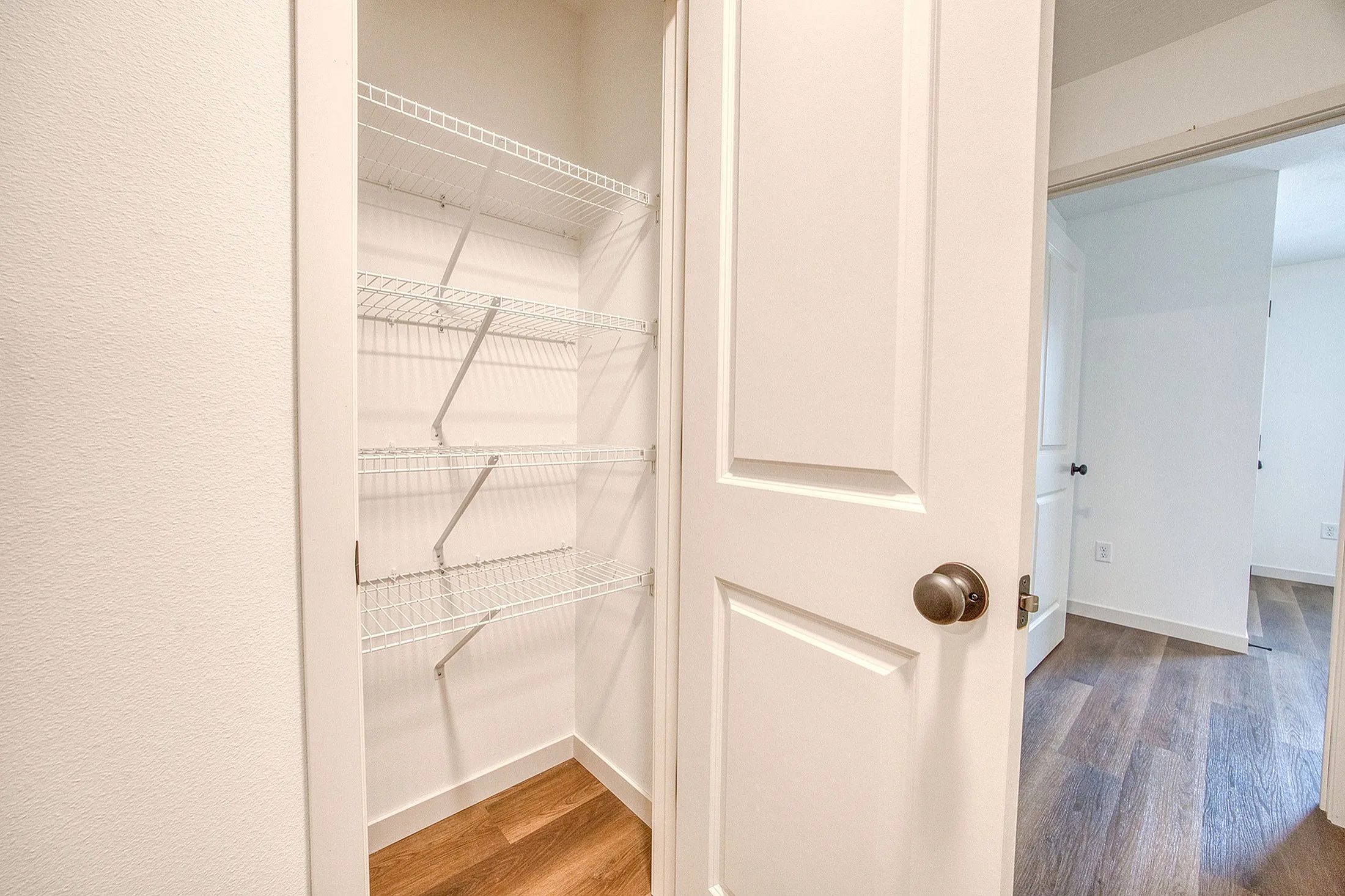 Spacious walk-in closet with sleek wire shelving and elegant hardwood flooring, designed for optimal organization and style.