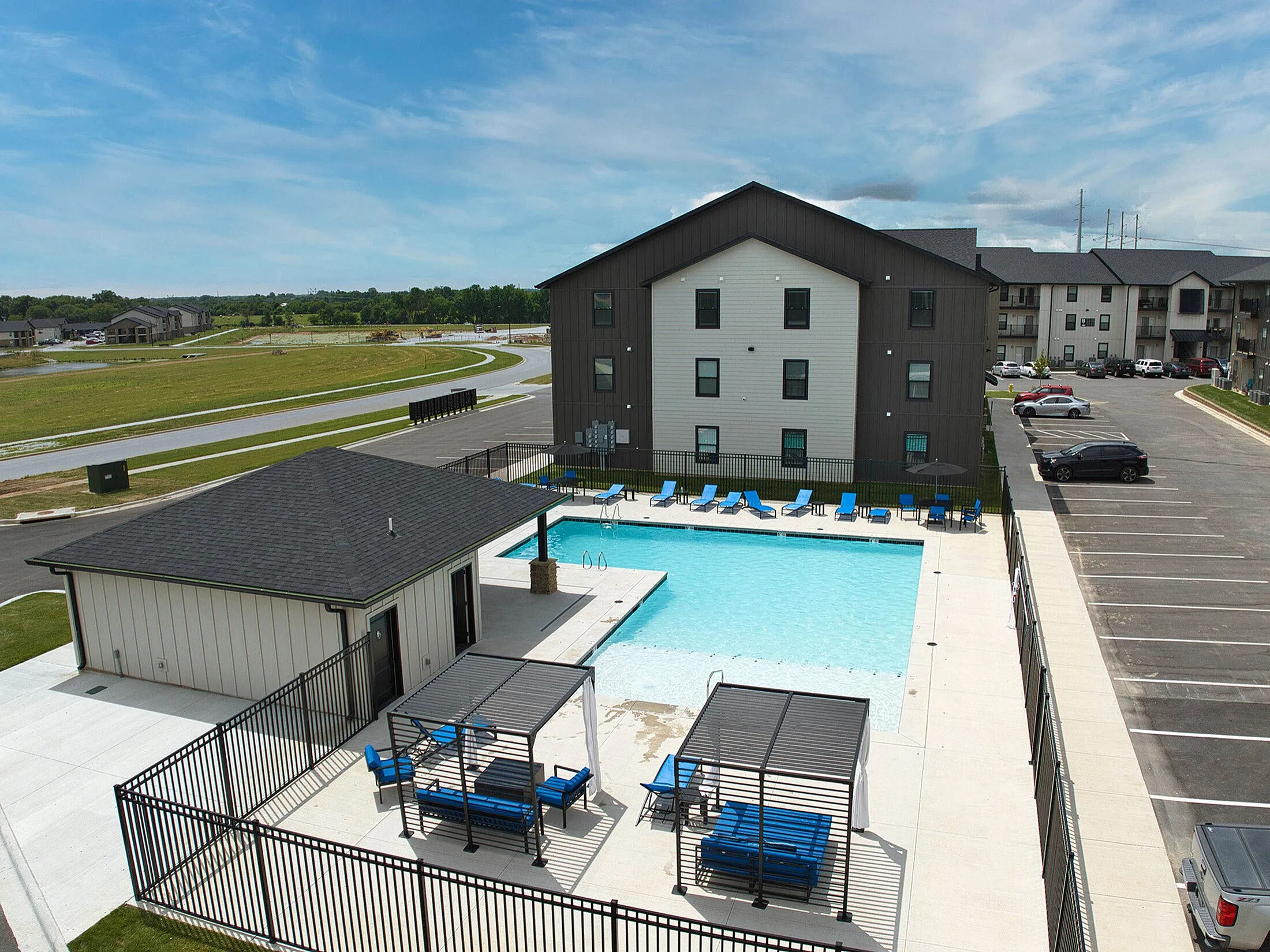 Vibrant apartment complex featuring a refreshing outdoor pool, spacious sun loungers, and modern architecture, set against a serene green landscape.