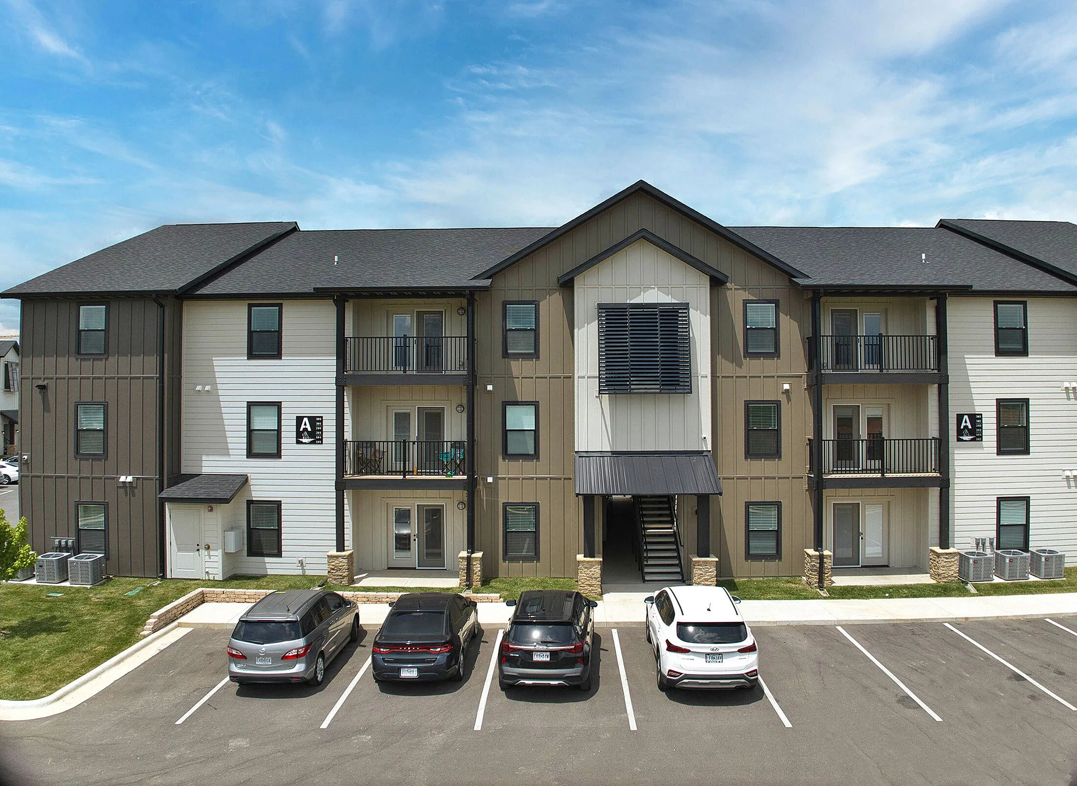 Modern apartment complex with a sleek exterior, featuring neutral colors and private balconies. Ample parking available for residents.