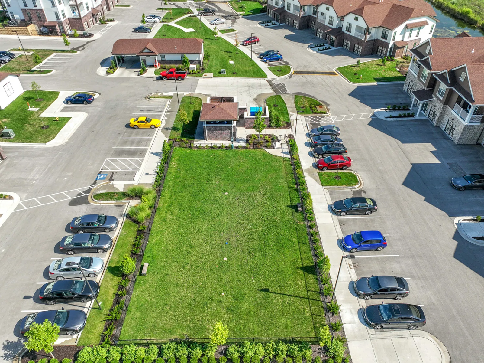 Aerial view of a modern apartment complex with lush green spaces, ample parking, and surrounding residential buildings.