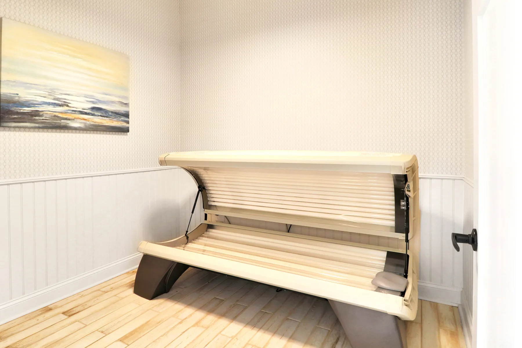 Bright and airy room with a modern tanning bed, complemented by a serene coastal painting and elegant white panel walls.