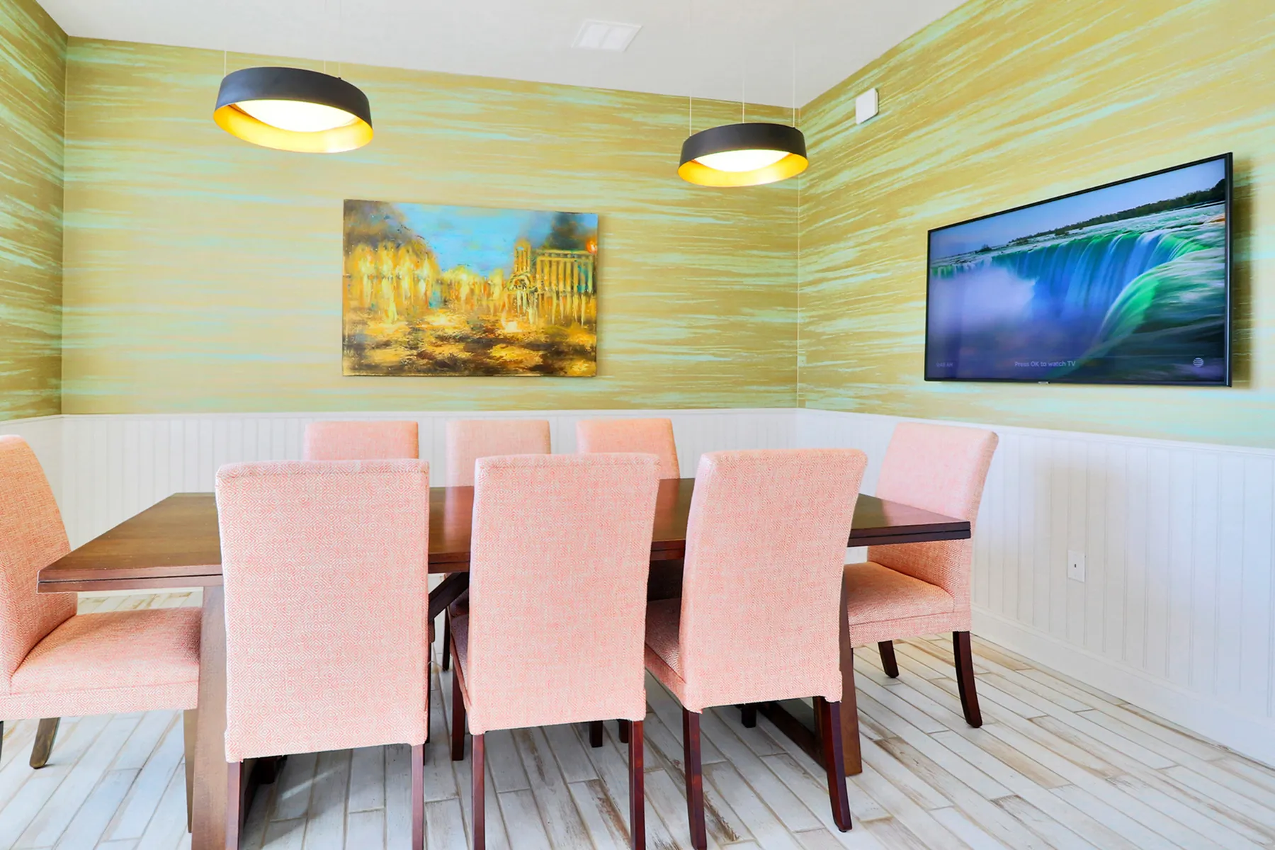Elegant dining area with contemporary lighting, pastel cushioned chairs, and vibrant wall art creating a warm ambiance.