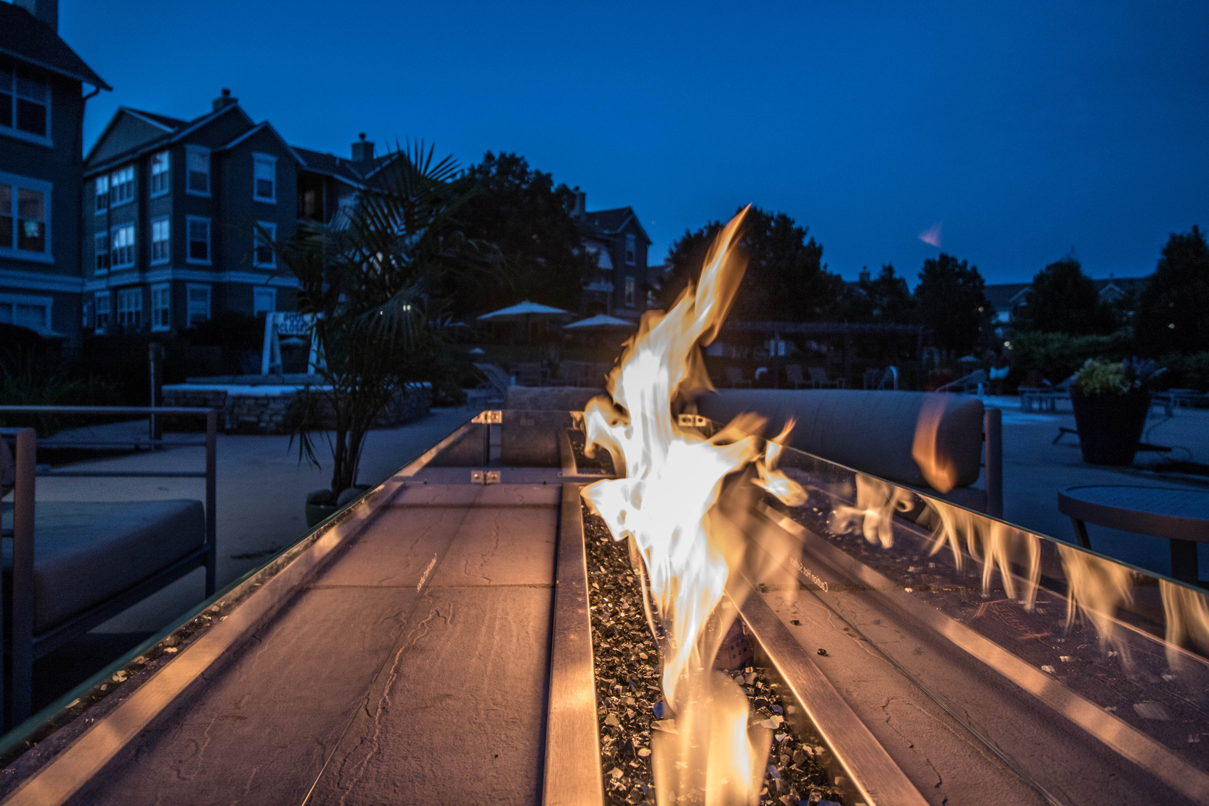 Elegant outdoor fire pit scene at a modern apartment complex, with cozy seating and a serene evening ambiance.