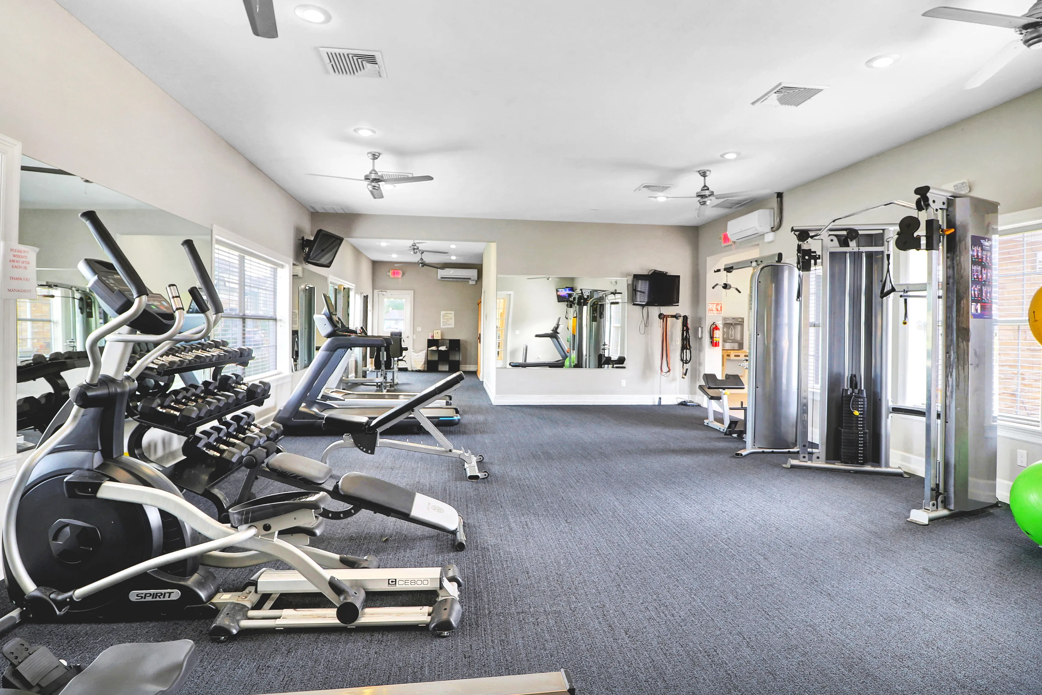 Modern fitness center with state-of-the-art exercise equipment, including treadmills, elliptical machines, and weight stations, in a bright and spacious setting.