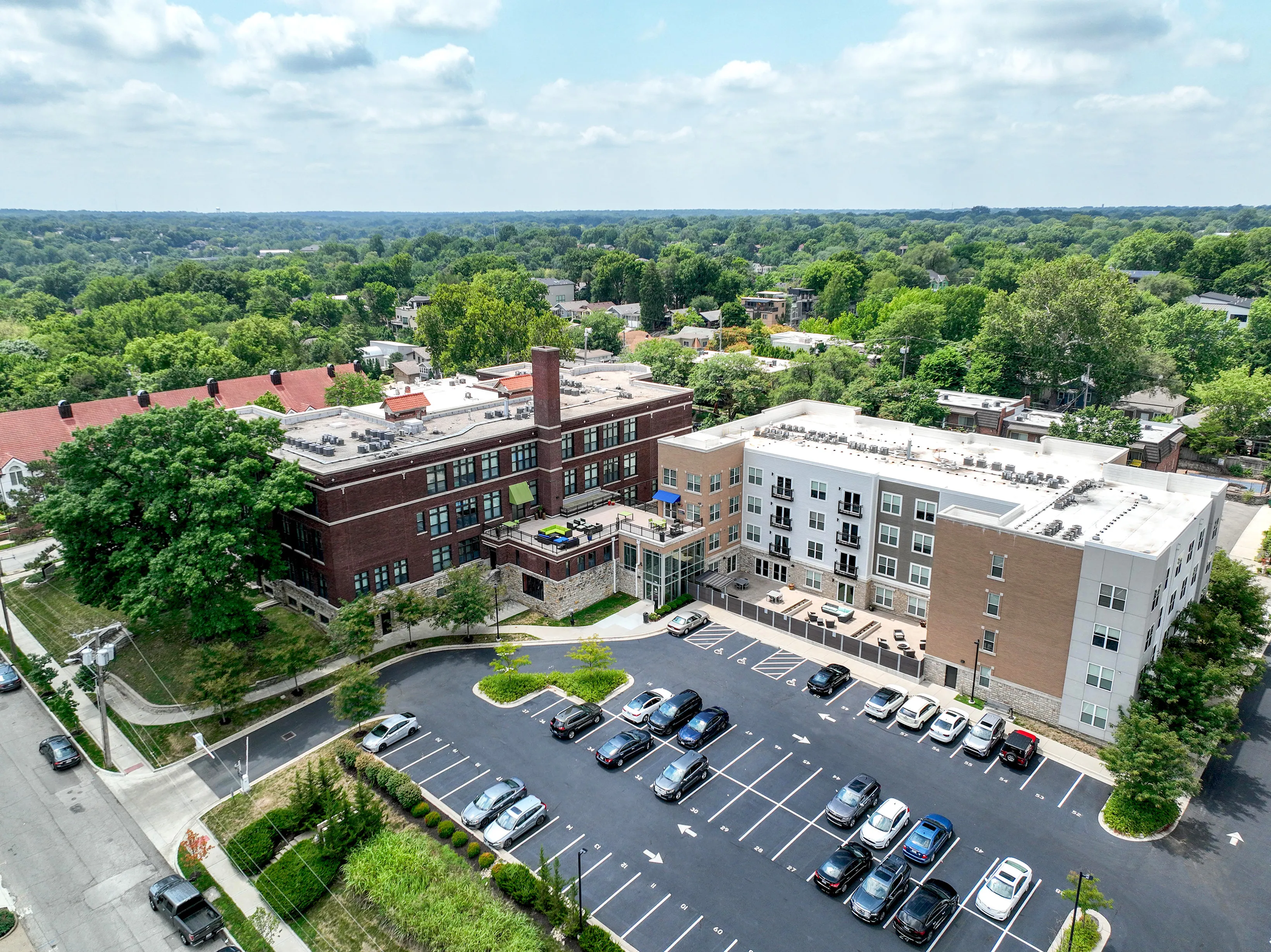 Charming aerial view of a modern apartment complex surrounded by lush greenery, featuring ample parking and attractive architecture.