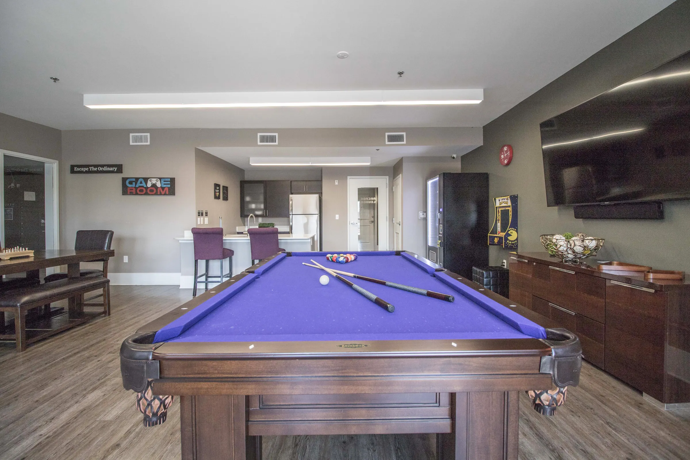 Luxurious modern game room with a sleek pool table, vibrant purple felt, and stylish kitchenette, perfect for entertainment and relaxation.