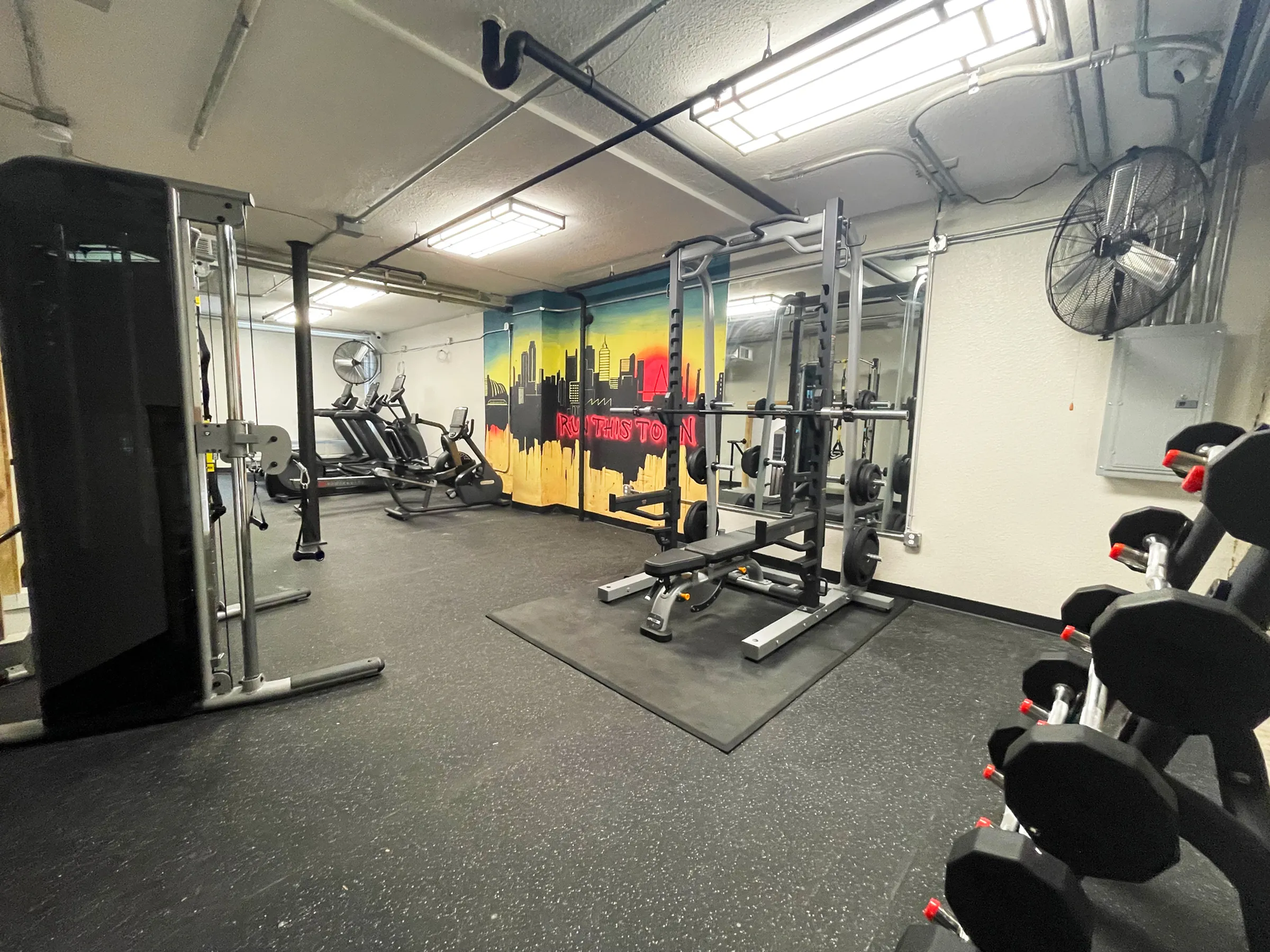 Contemporary fitness center with modern equipment, vibrant mural, and spacious workout area.
