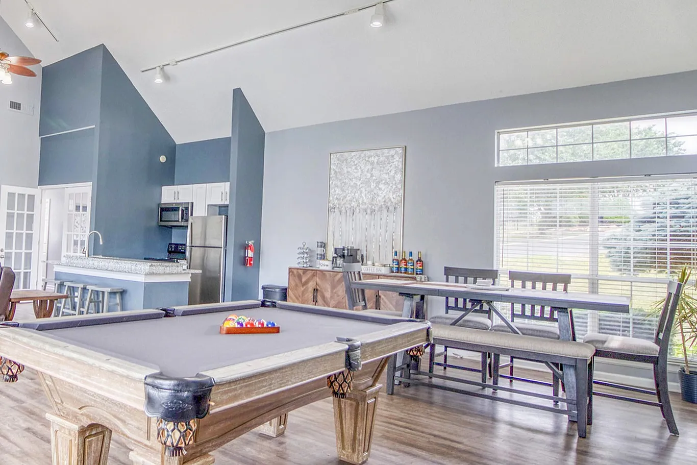 Spacious and modern living area with high ceilings, featuring a stylish pool table, cozy seating, and a sleek kitchen. Large windows bring in natural light for a bright and inviting space.