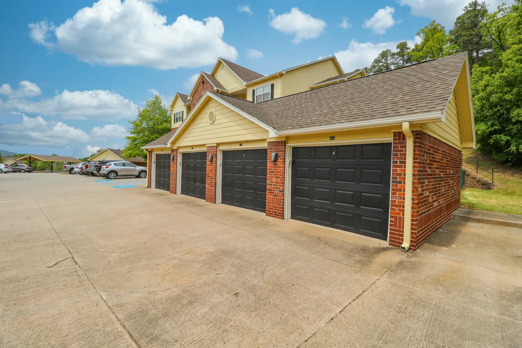 Charming duplex with modern black garage doors, nestled in a tranquil neighborhood with lush greenery and a clear blue sky.