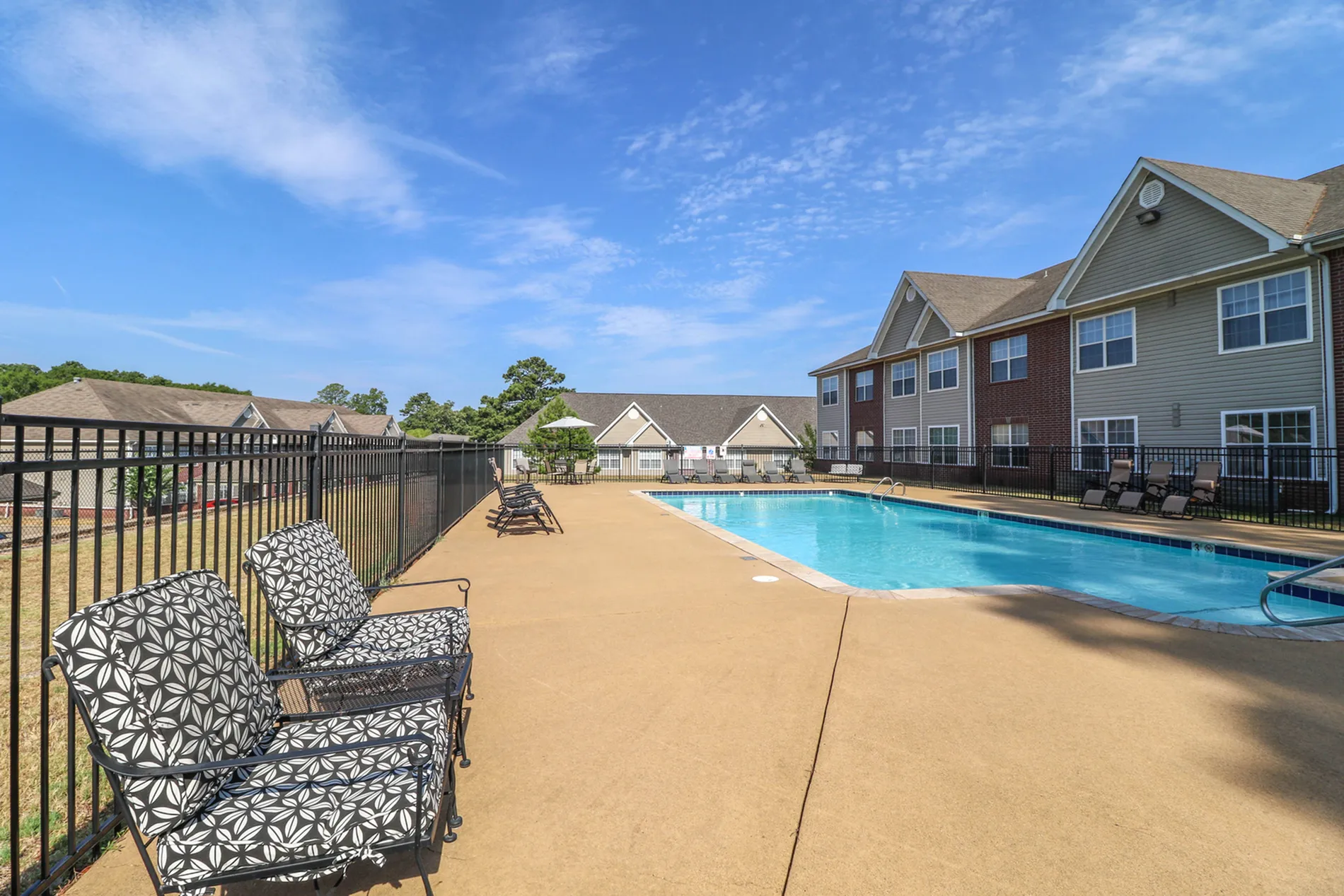 Inviting apartment pool area with elegant lounge chairs, clear blue skies, and cozy seating, perfect for relaxation.