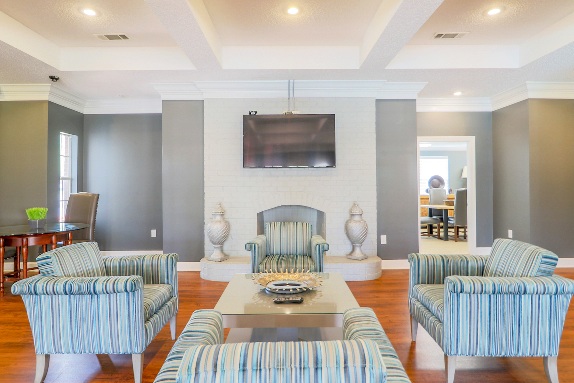 Chic living room with striped armchairs, elegant coffered ceiling, and a wall-mounted TV, exuding modern sophistication.