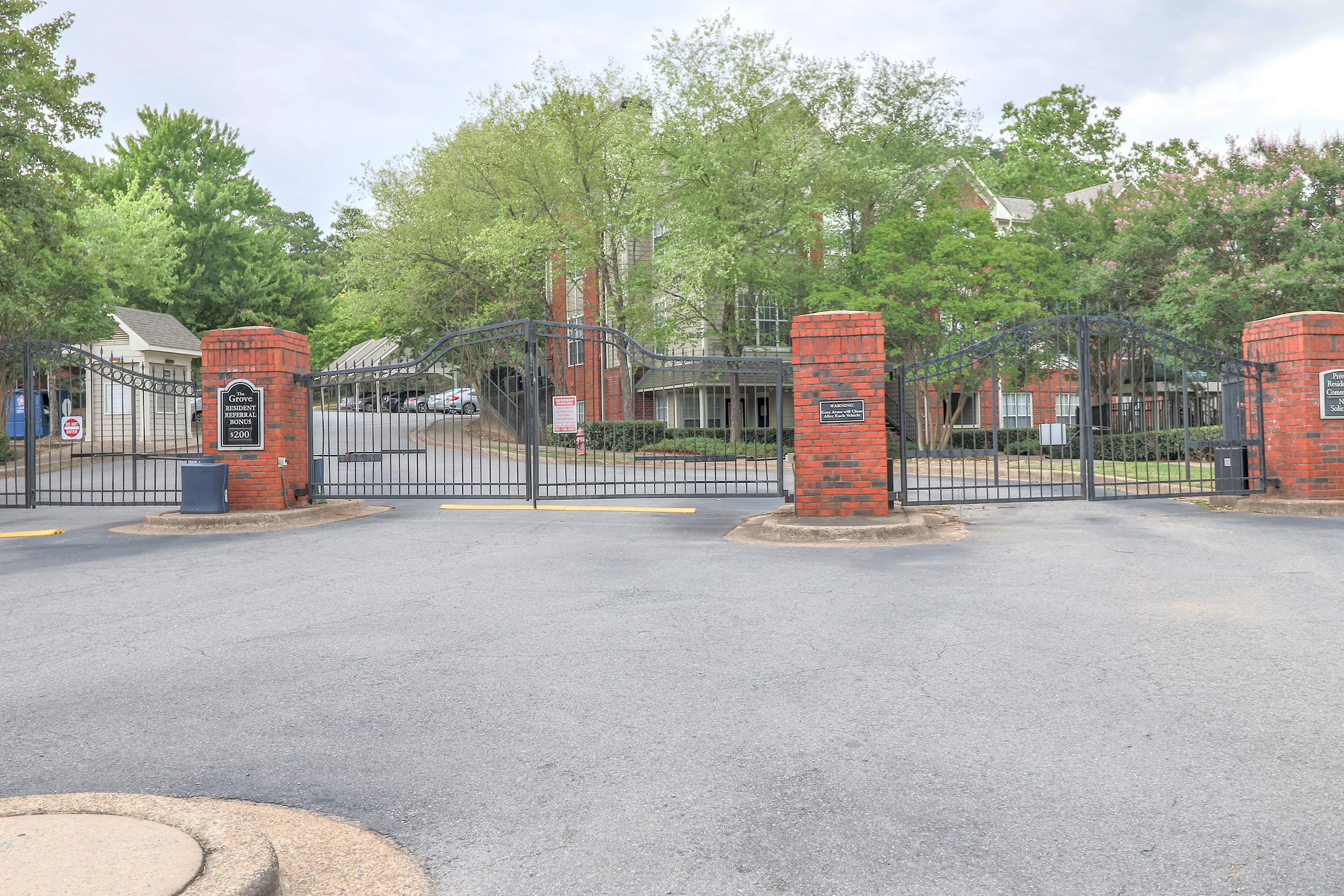 Inviting gated entrance of a serene apartment community, surrounded by lush greenery and framed by elegant brick pillars.