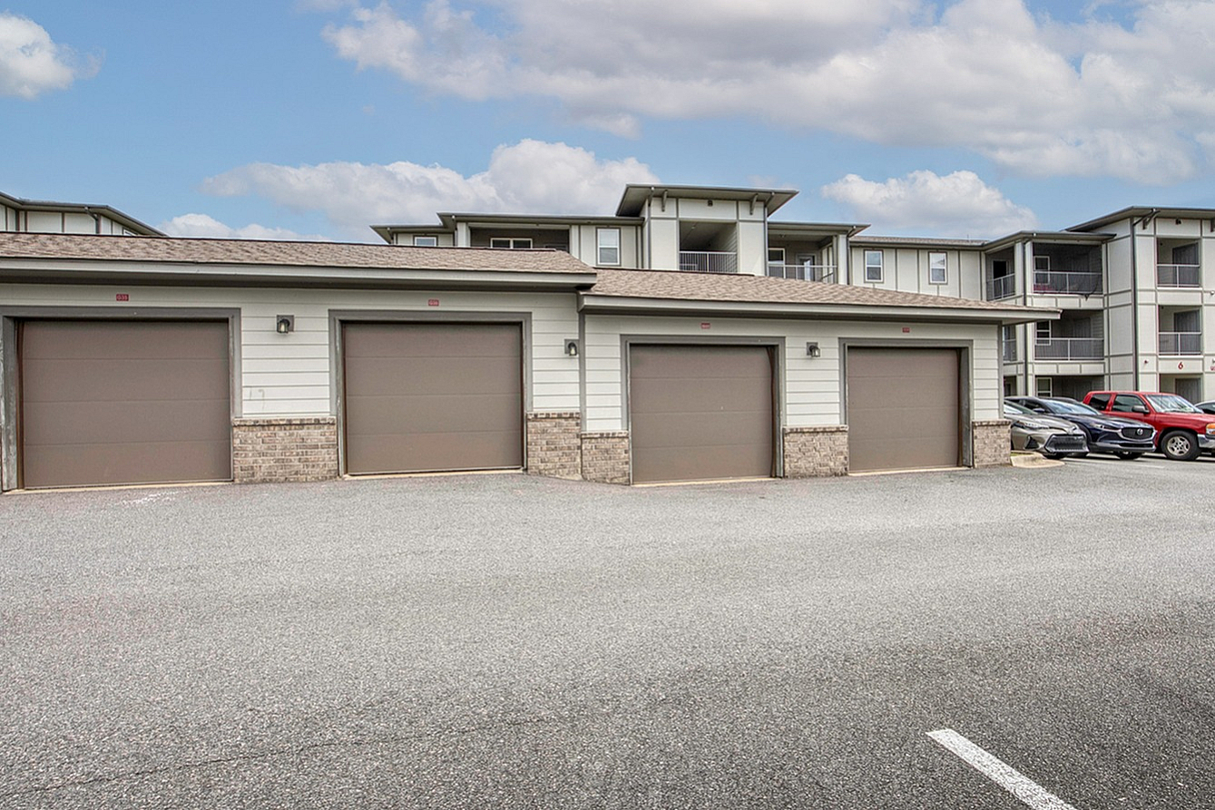 Modern apartment complex with attached garages under a bright blue sky, offering ample parking and stylish architecture.