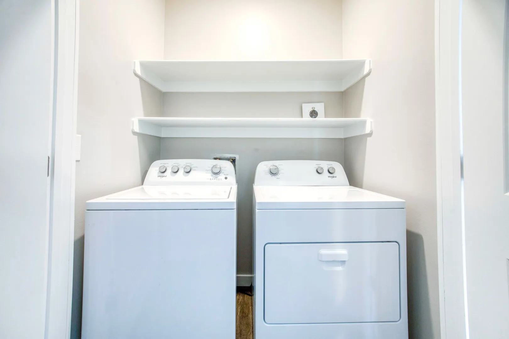 Modern laundry space featuring sleek washer and dryer set with convenient overhead shelving for storage.