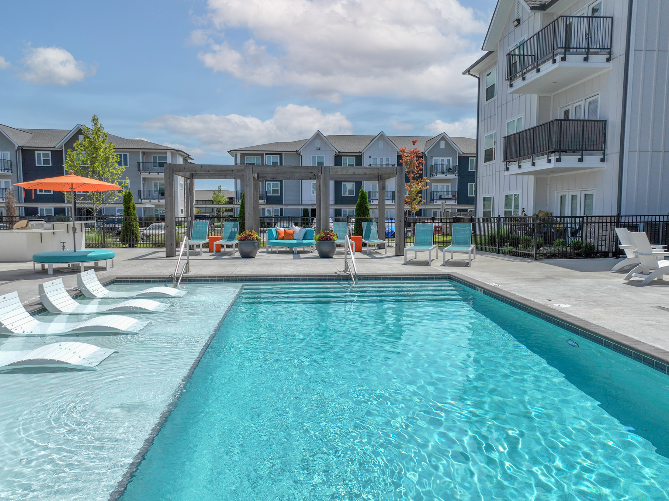 Luxurious apartment complex featuring a pristine outdoor pool, stylish lounging chairs, and modern architecture under a clear blue sky.
