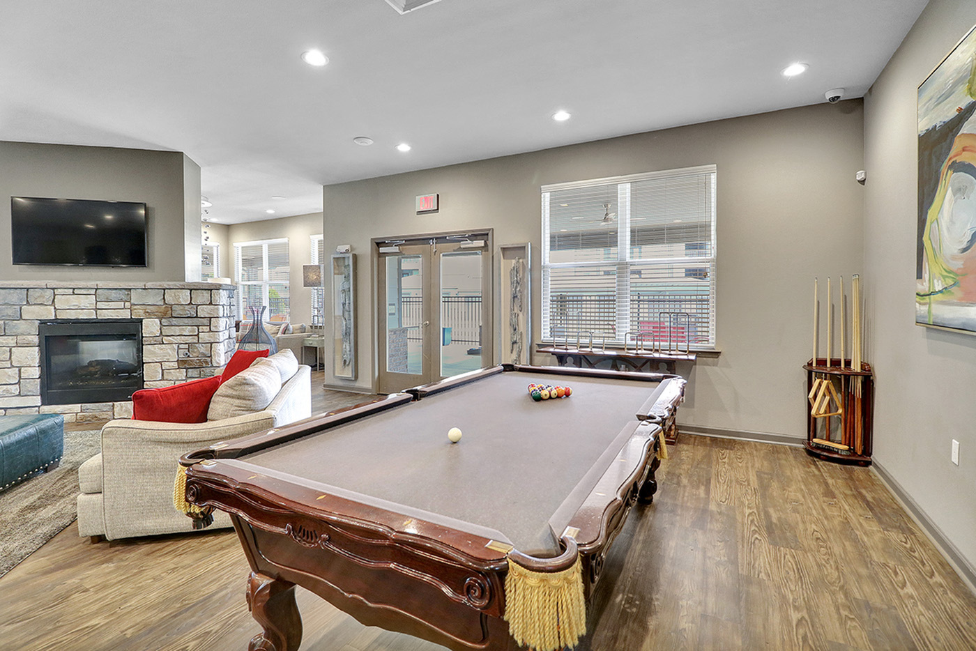 Inviting recreational room with a sleek pool table, cozy sofa, stone fireplace, and large windows offering natural light.