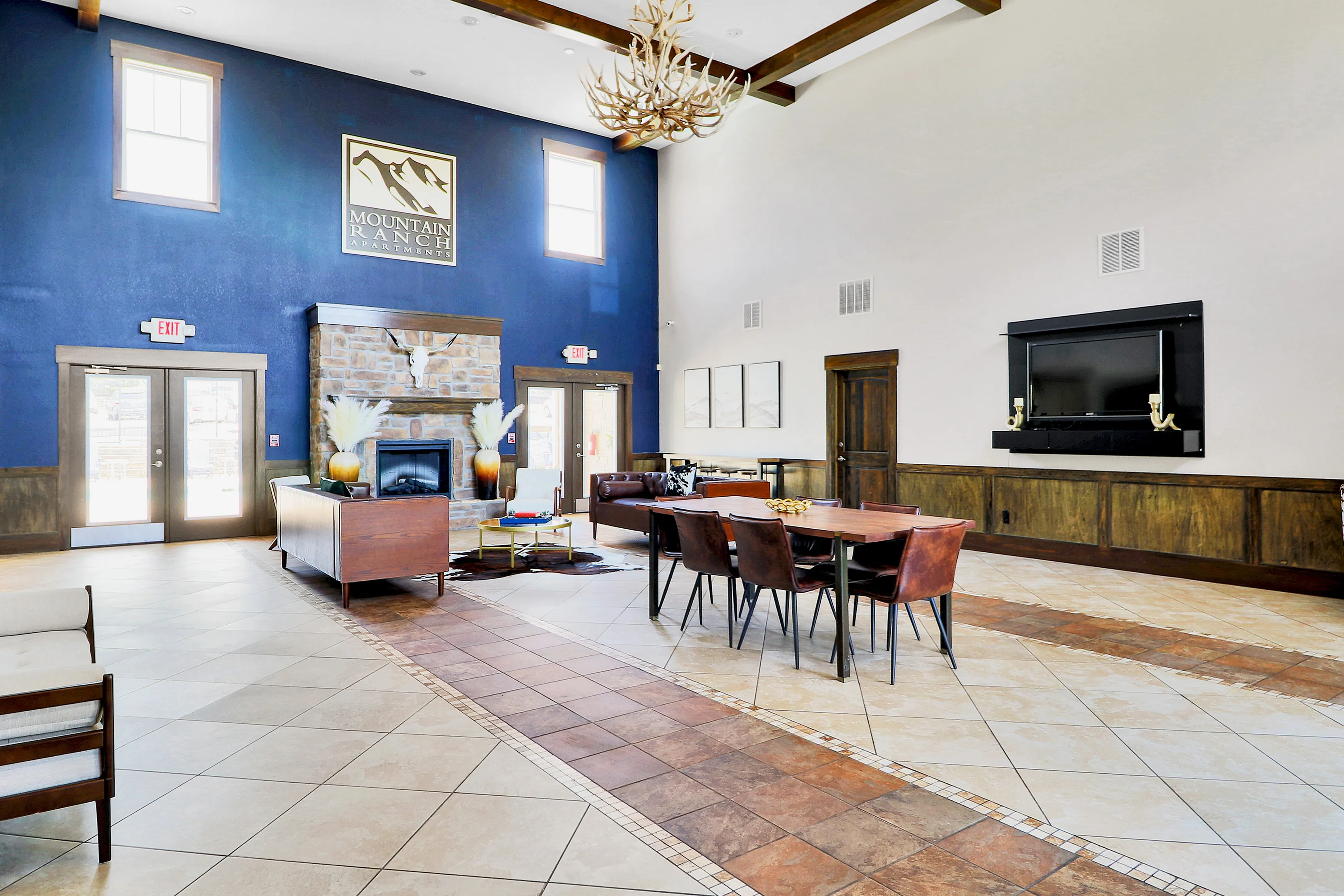 Spacious and elegant community room at Mountain Ranch Apartments, featuring a cozy stone fireplace, stylish seating, and modern decor under high ceilings.