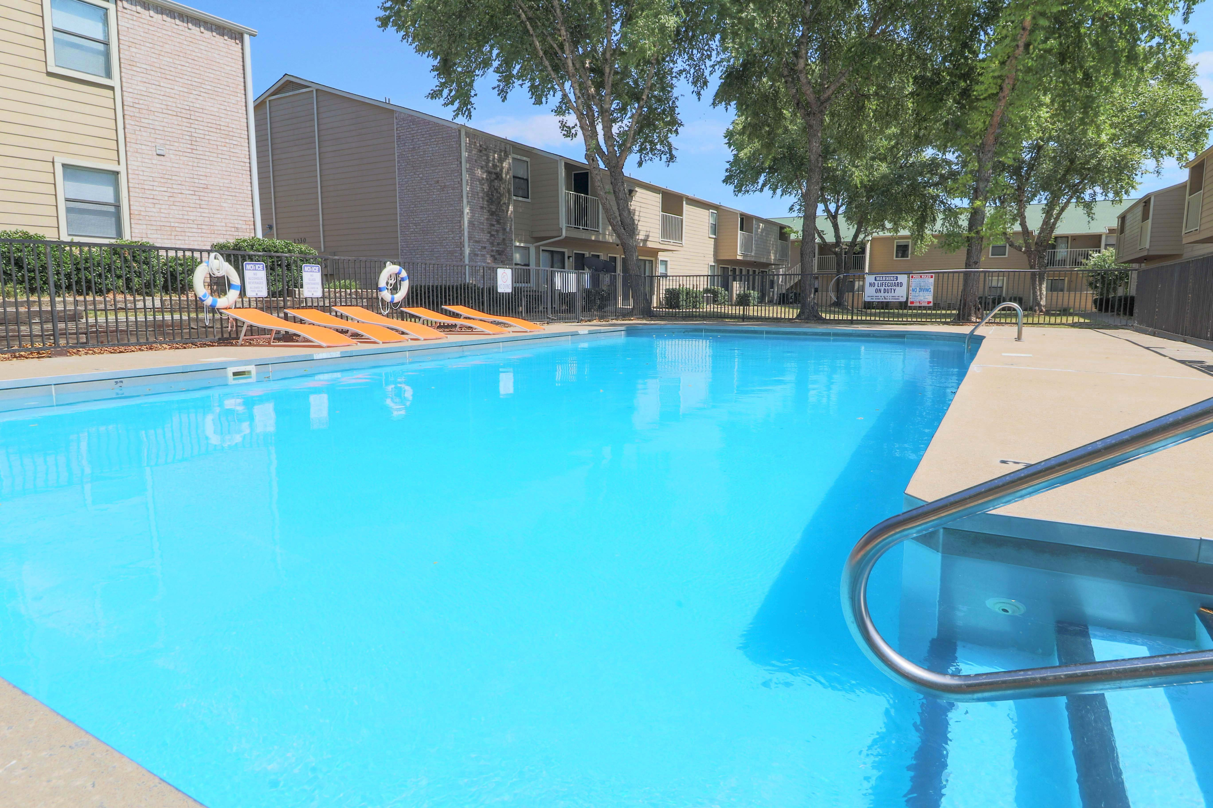 Inviting outdoor pool with crystal-clear water, set amidst modern apartment buildings and lush greenery, perfect for relaxation and leisure.