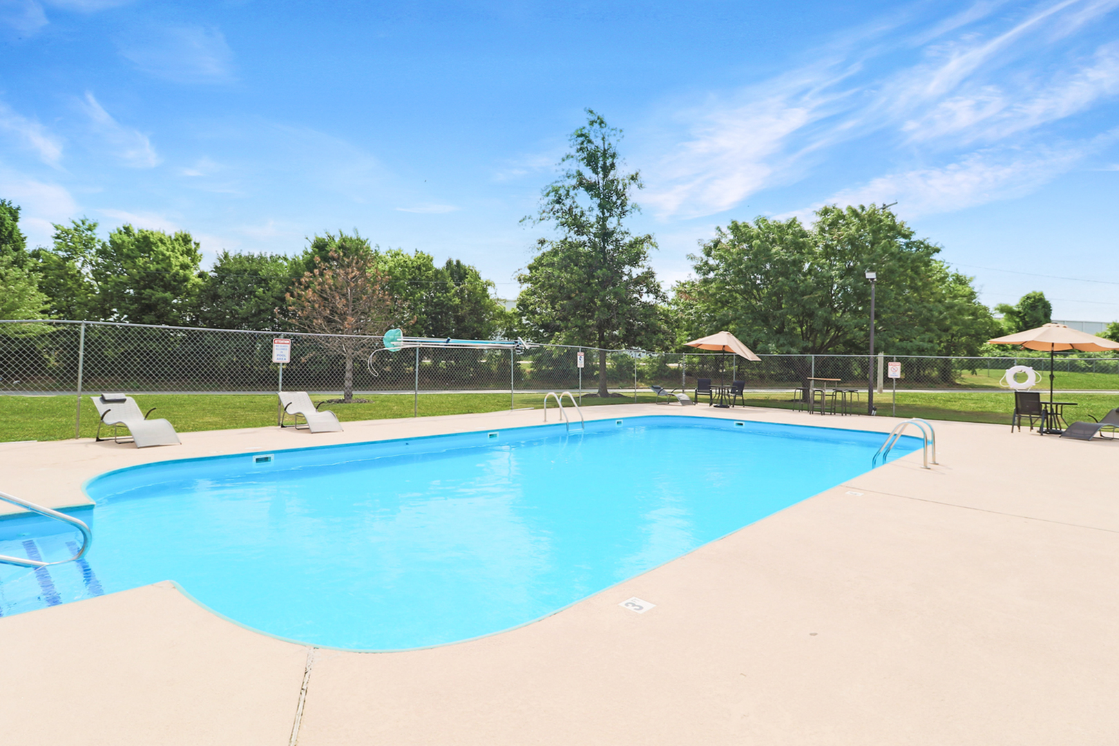 Inviting outdoor pool area with lounge chairs and umbrellas, surrounded by lush greenery under a bright blue sky.