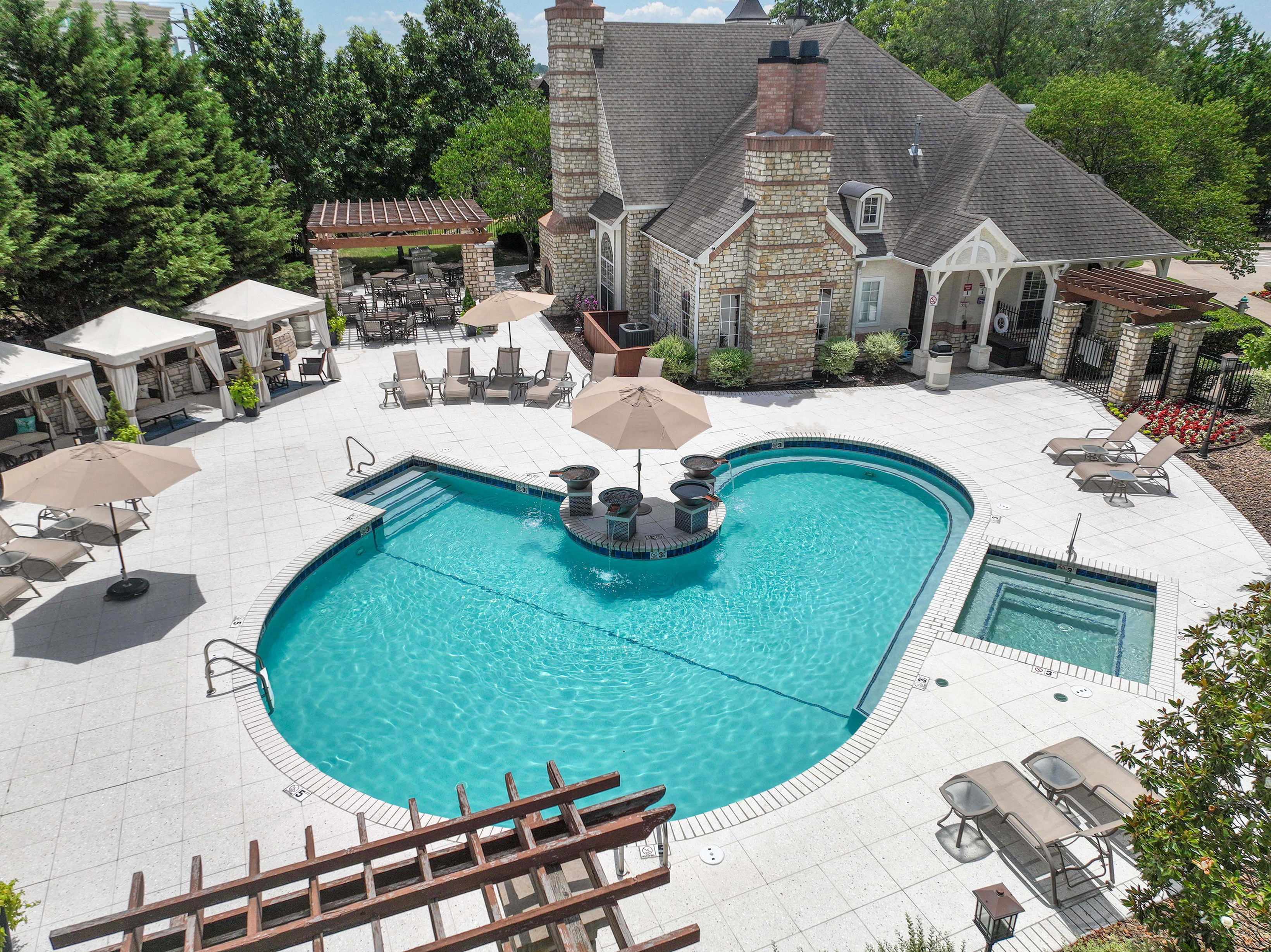 Luxurious outdoor pool area featuring a resort-style swimming pool, elegant lounge chairs, and charming stone-clad architecture with lush greenery.