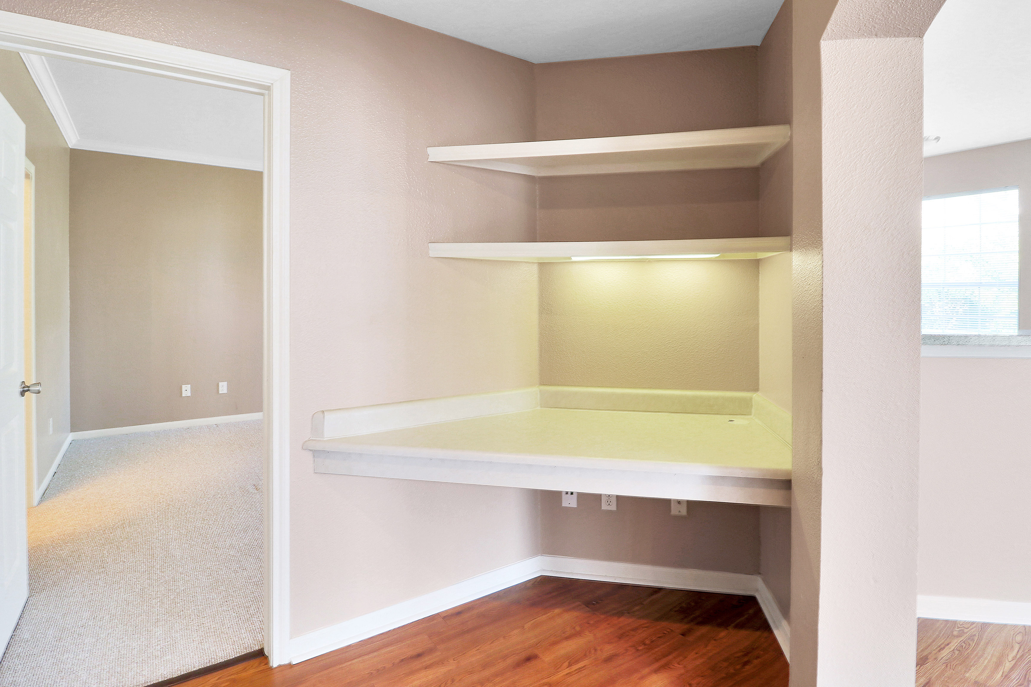 Modern apartment nook with built-in shelves and cozy workspace, featuring soft lighting and elegant wooden flooring.