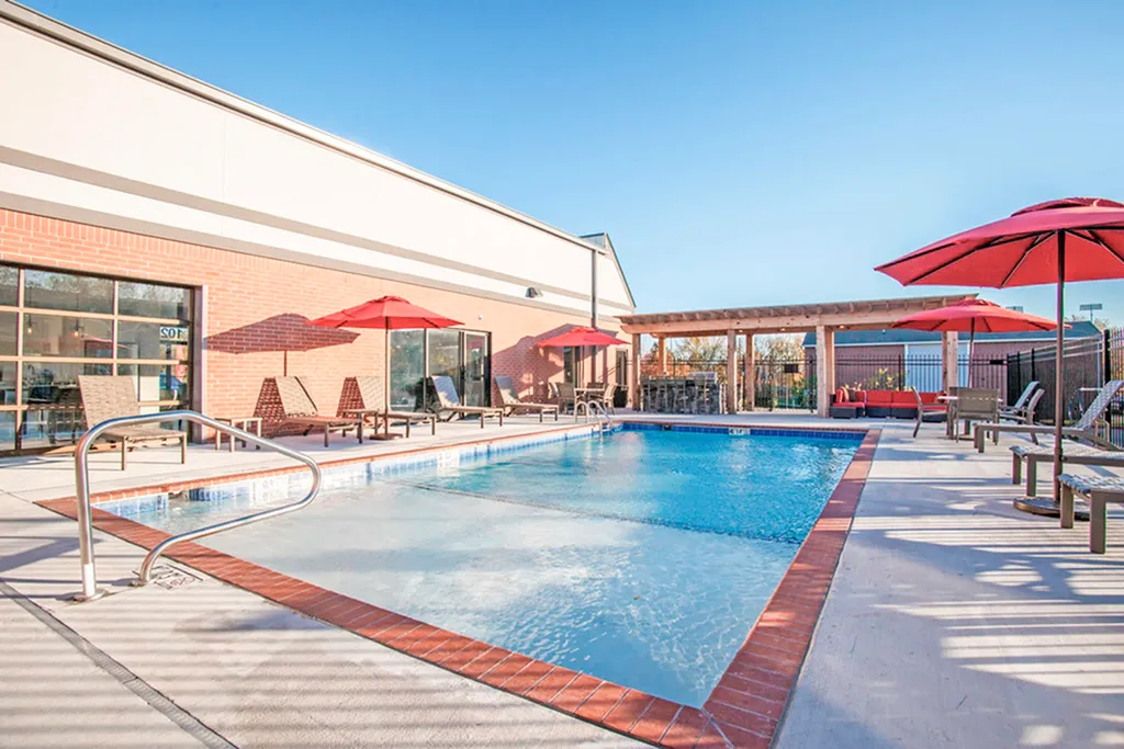 Inviting outdoor pool area with luxurious lounge chairs and vibrant red umbrellas, perfect for relaxation under a clear blue sky.