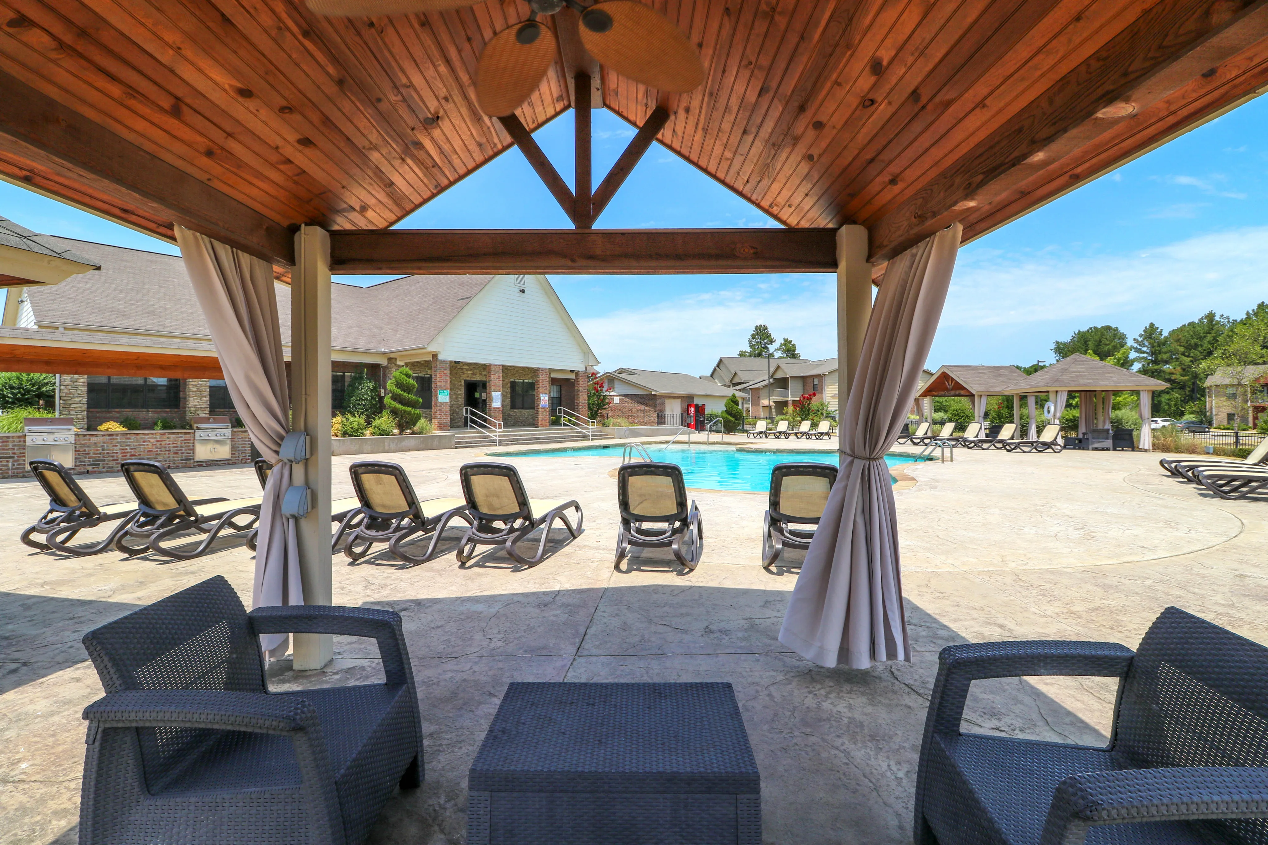 Inviting poolside oasis with comfortable loungers, shaded seating, and a modern clubhouse backdrop for ultimate relaxation.