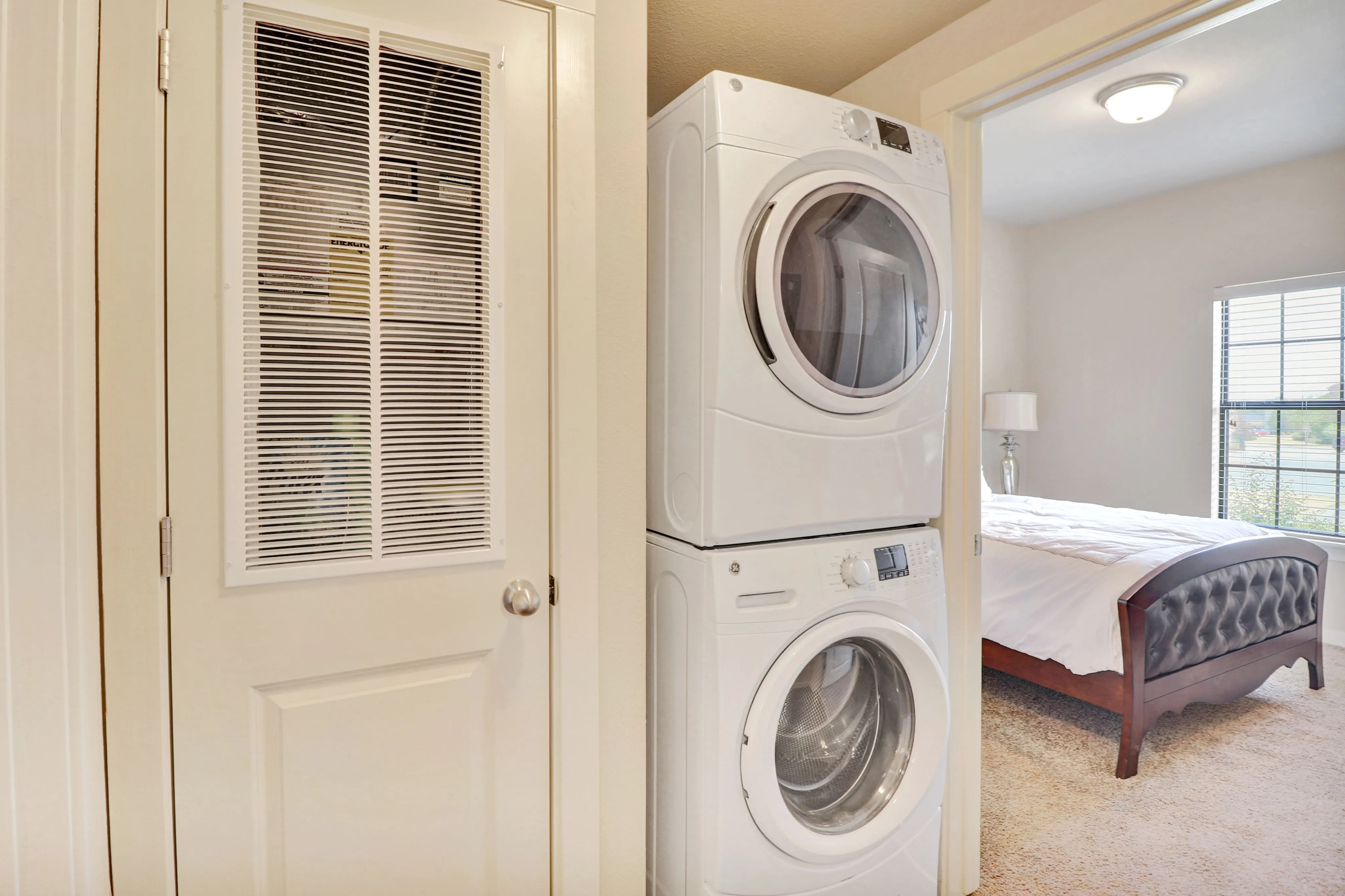 Modern apartment featuring an in-unit stacked washer and dryer beside a bright, airy bedroom with plush carpeting.